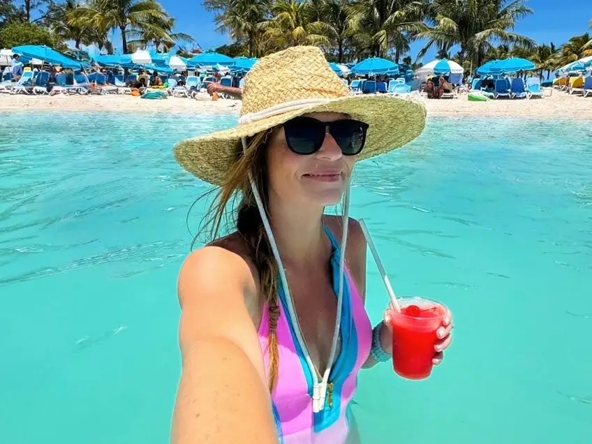 Emily holds a drink in the ocean while wearing a hat and sunglasses.