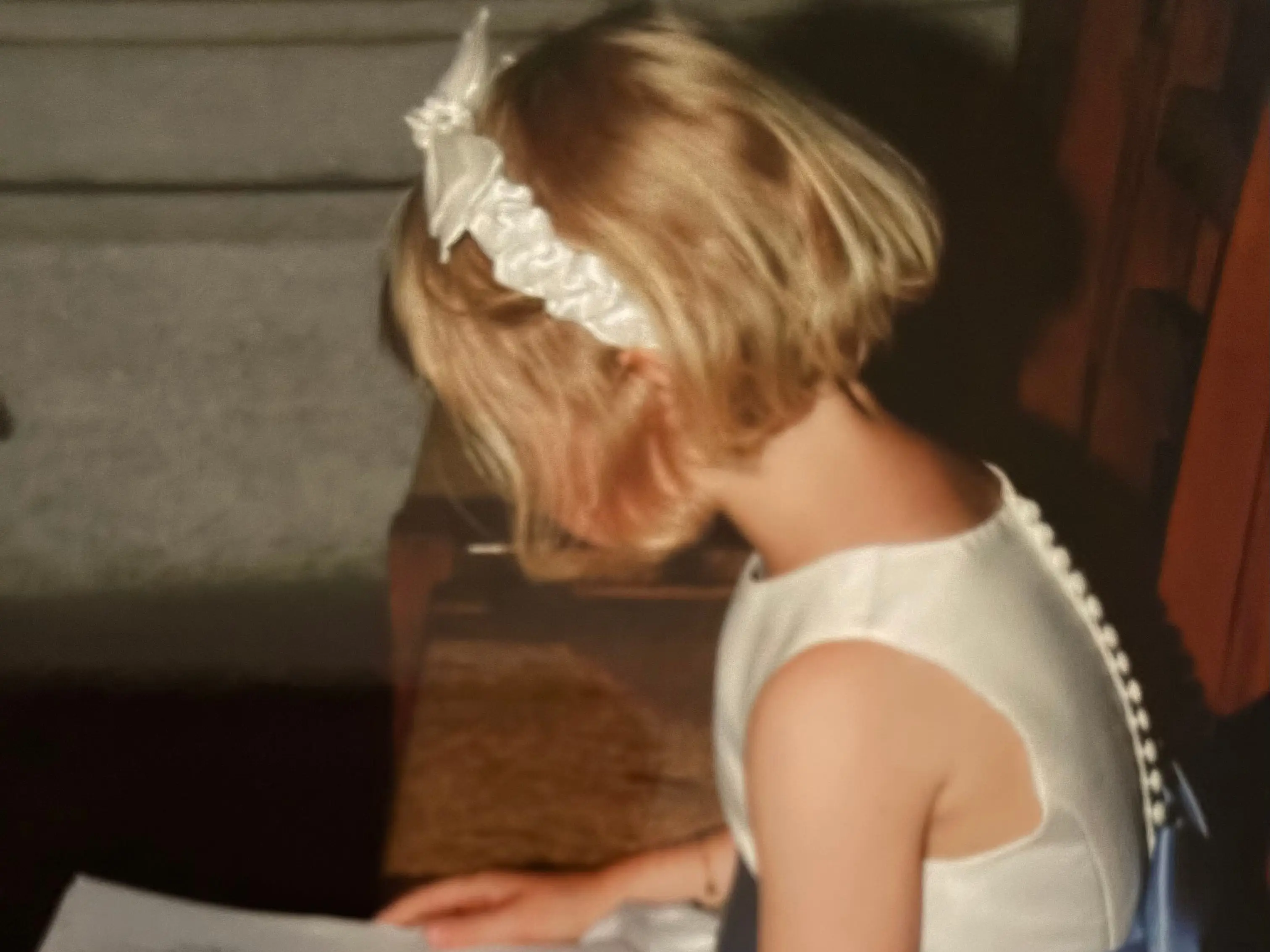 A little girl in a white dress and a blue sash sitting on a chair