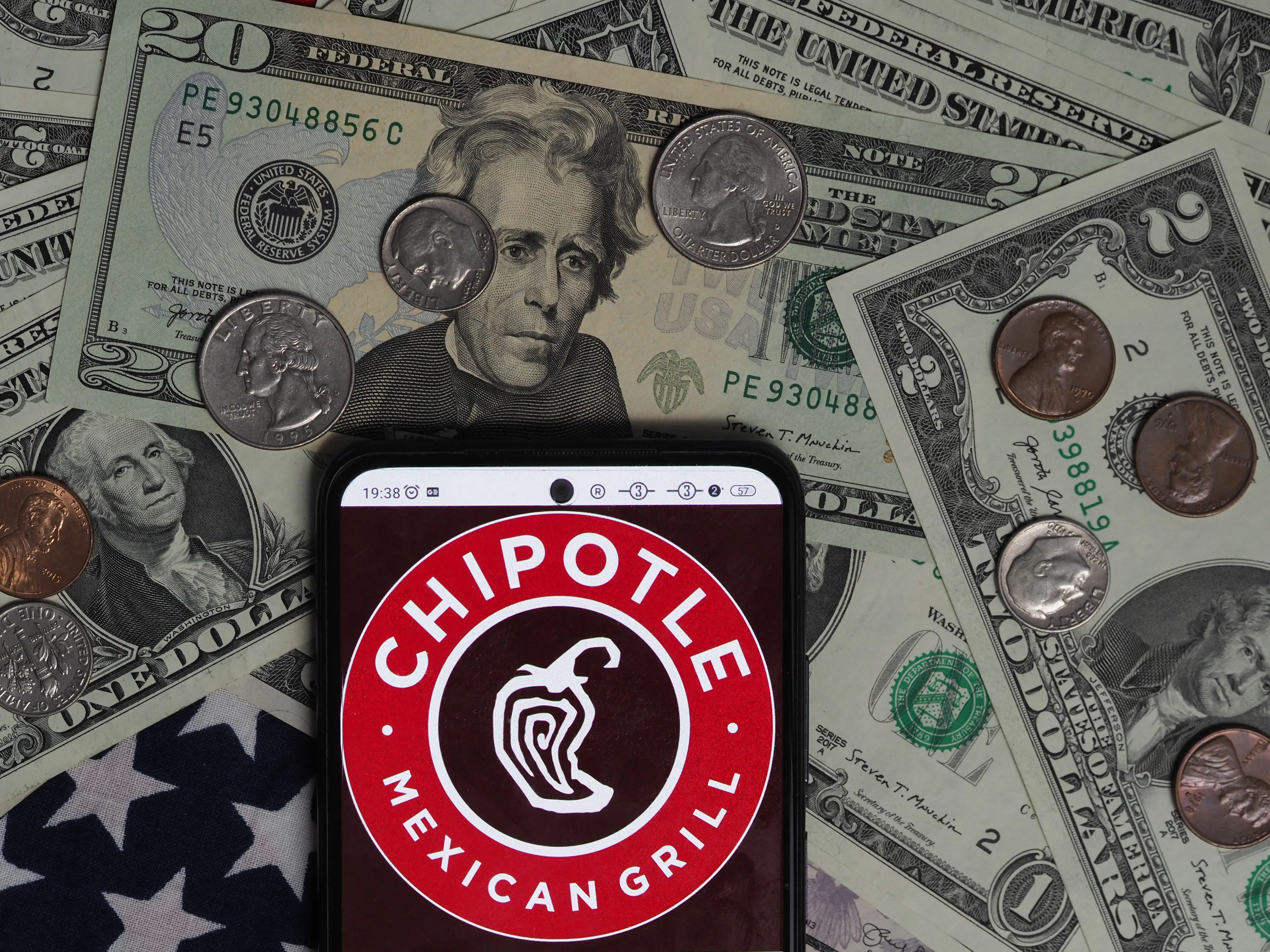 The Chipotle logo appears displayed on a cell phone laying on top of a pile of money.