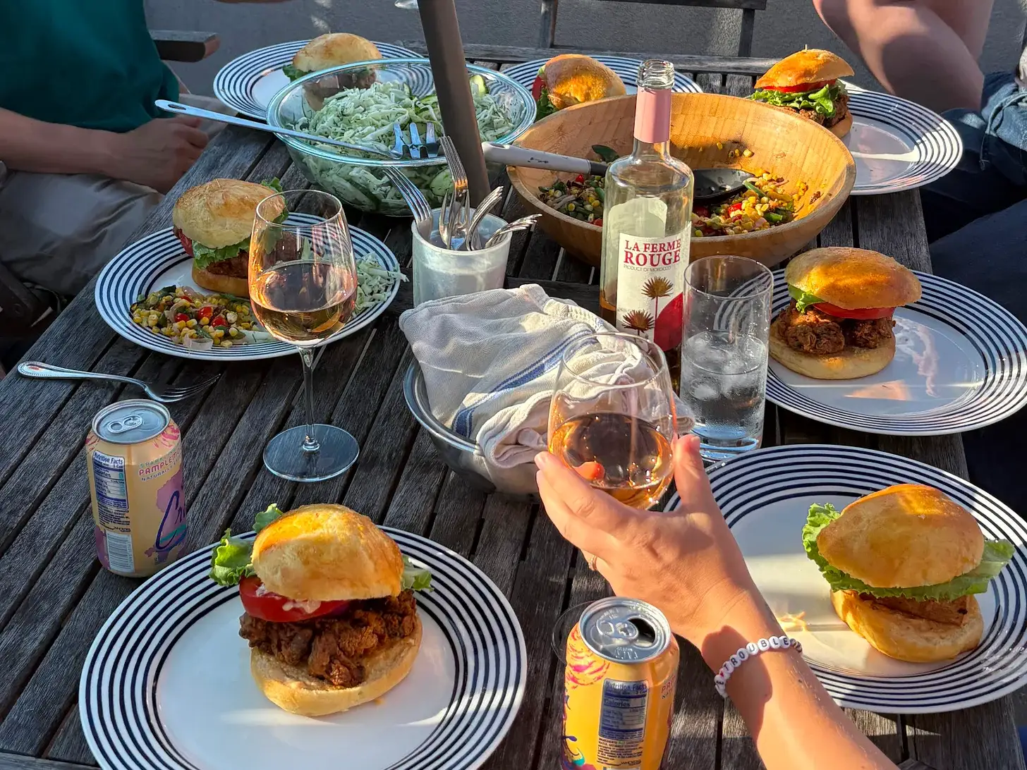 A dinner party table covered in plates of burgers, salad, and wine glasses.