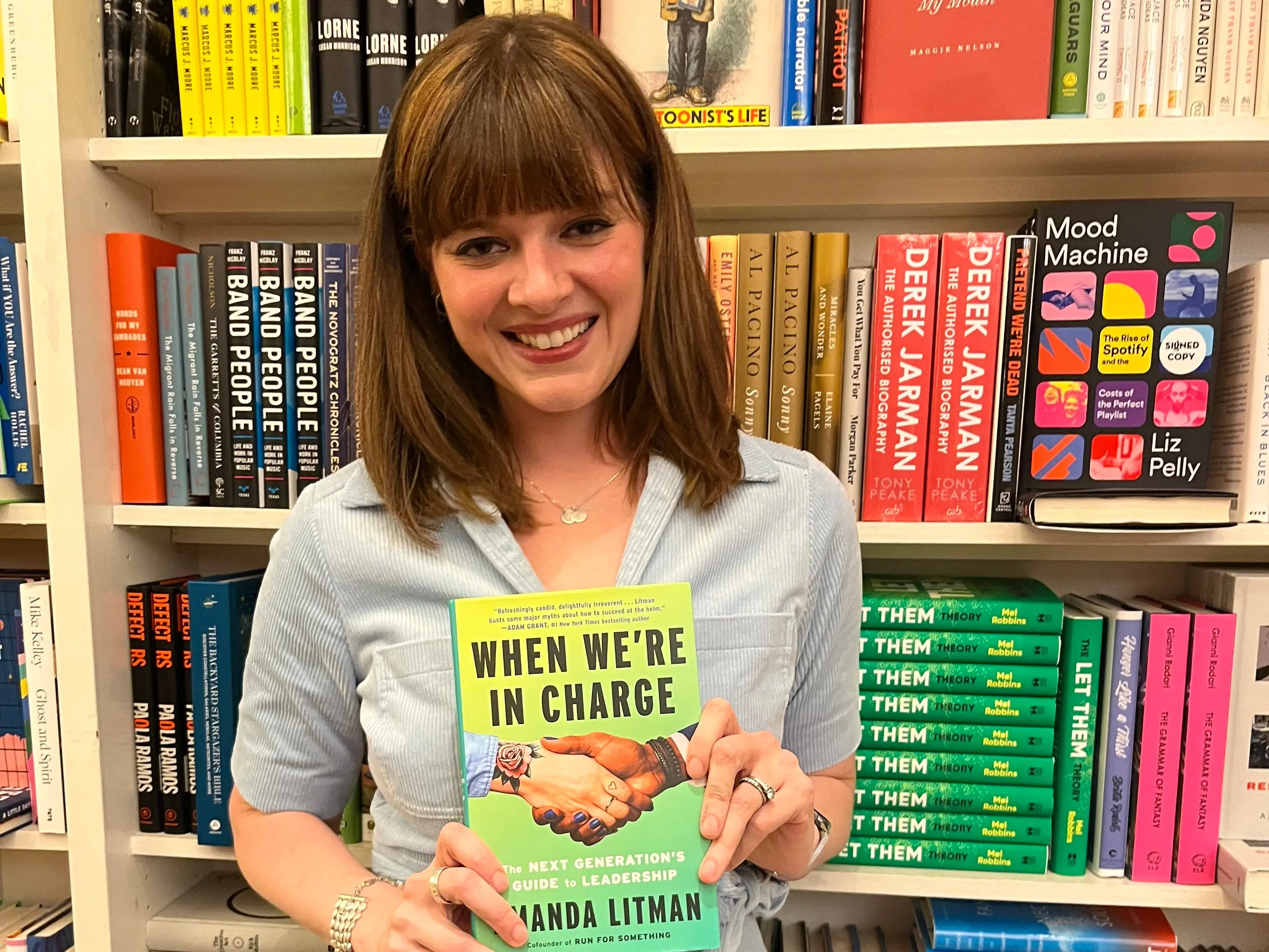 A woman standing in front of a bookshelf holds a book.