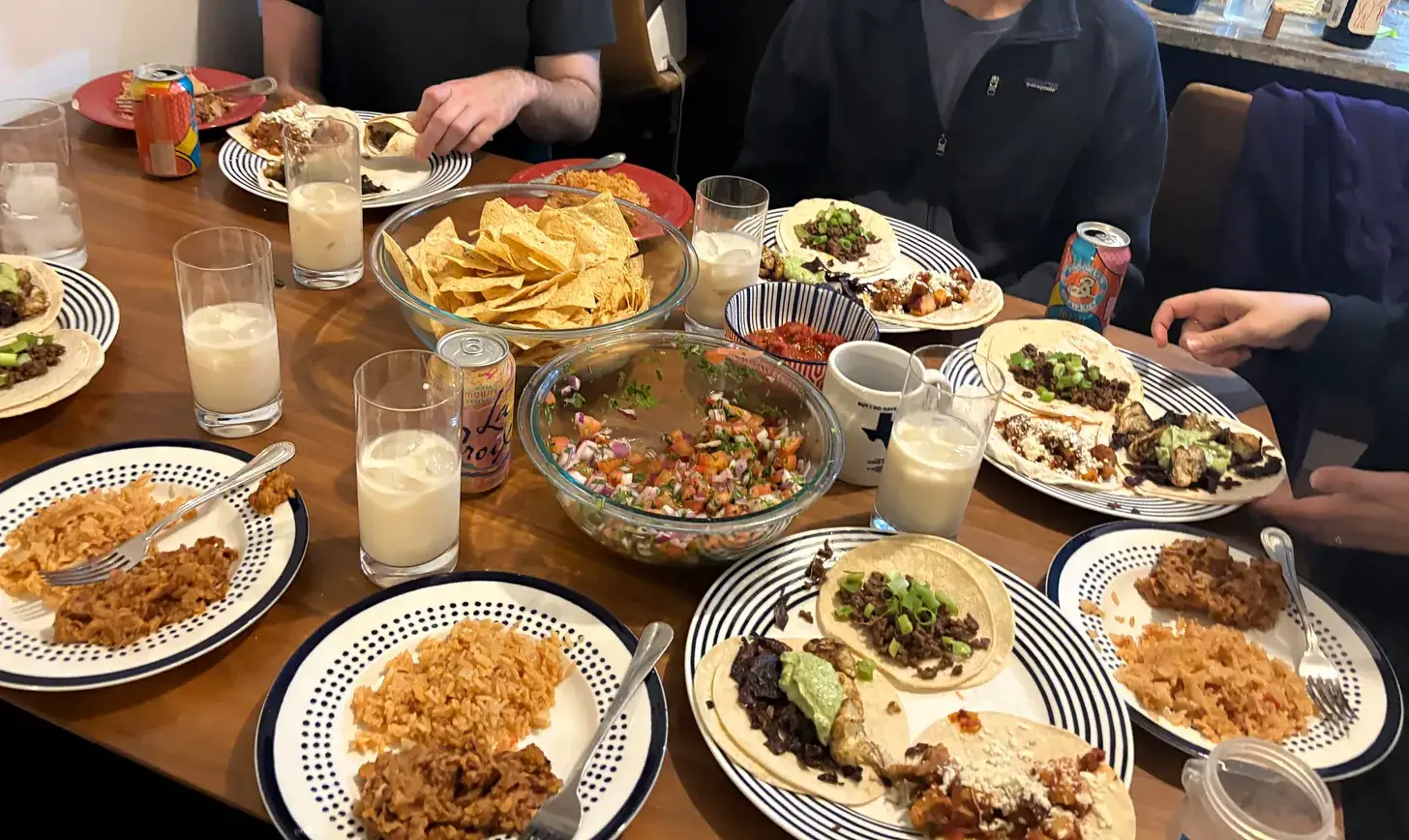 A dinner table covered with plates, tacos, tortilla chips, and drinks.