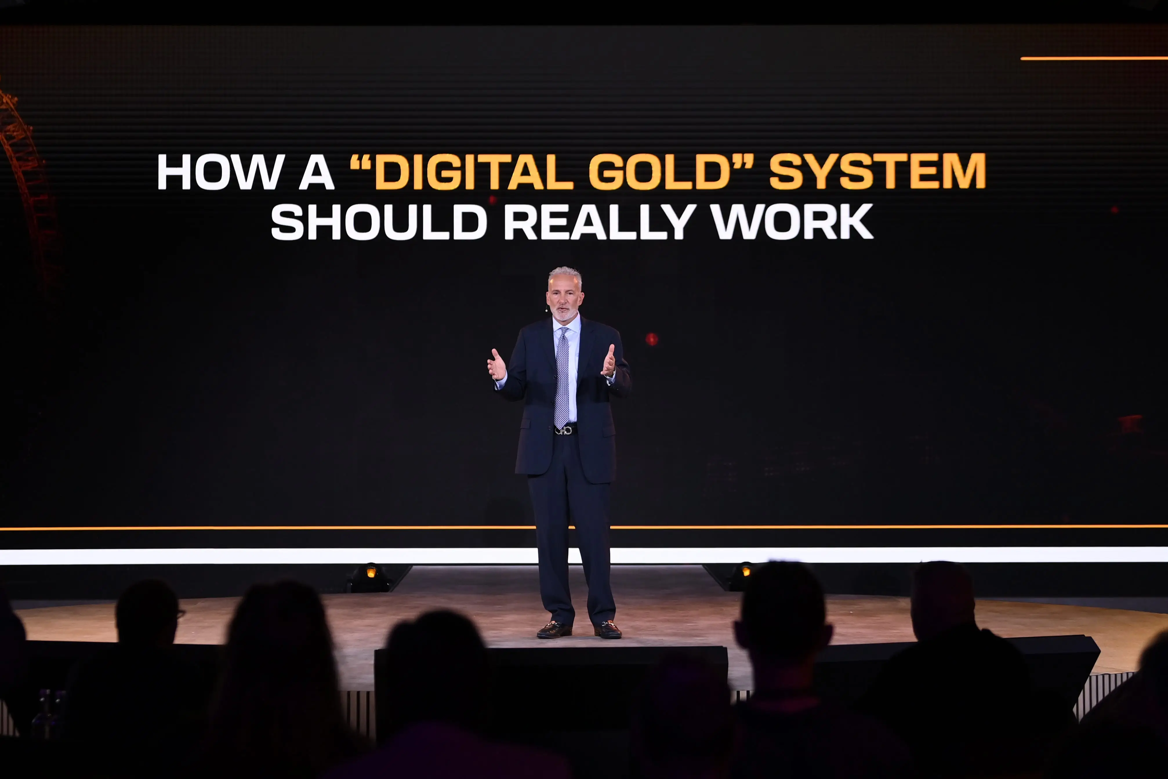 Peter Schiff speaks onstage at a conference with a PowerPoint reading 