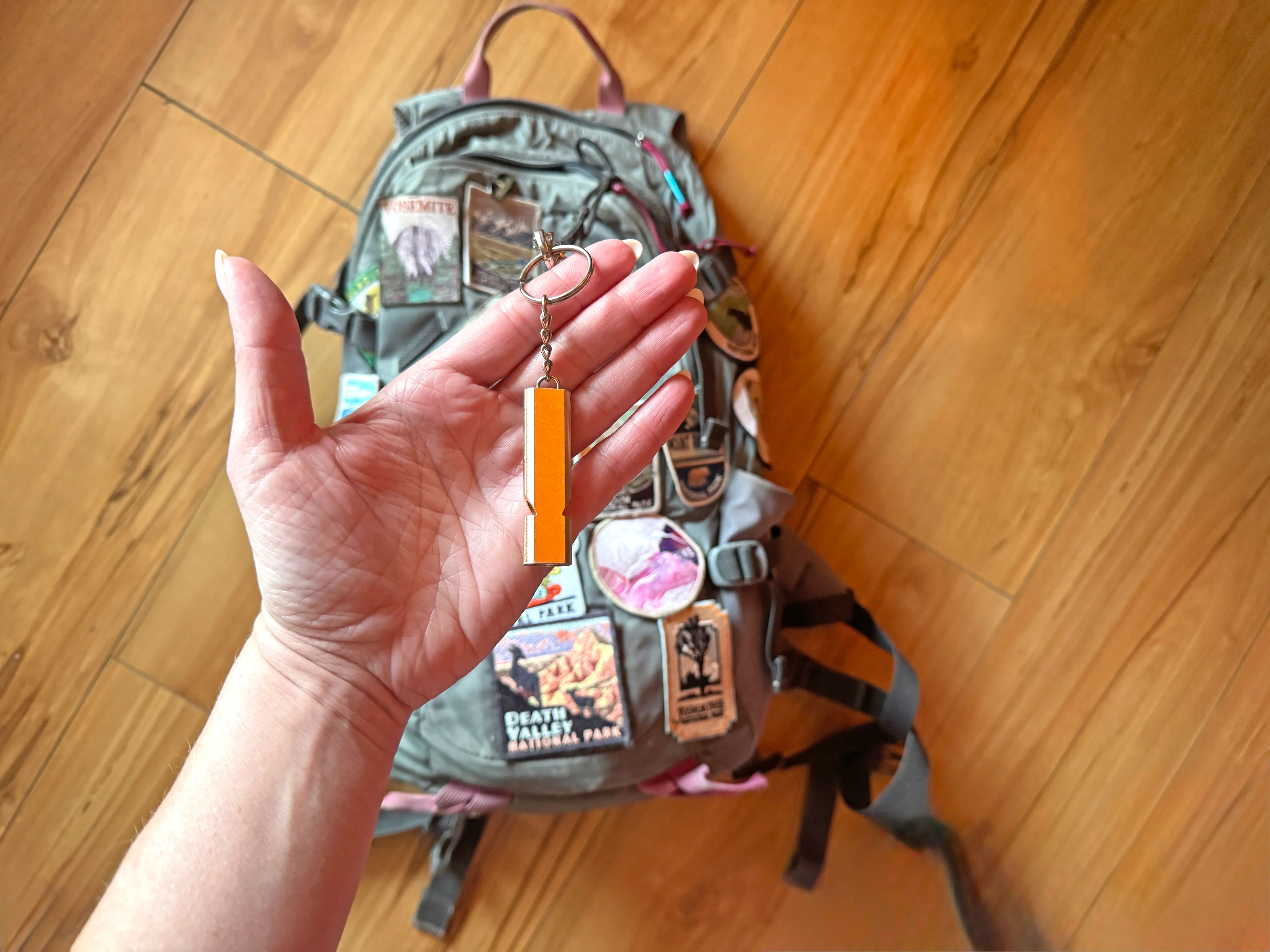 Emily holds a whistle over a backpack covered in patches.