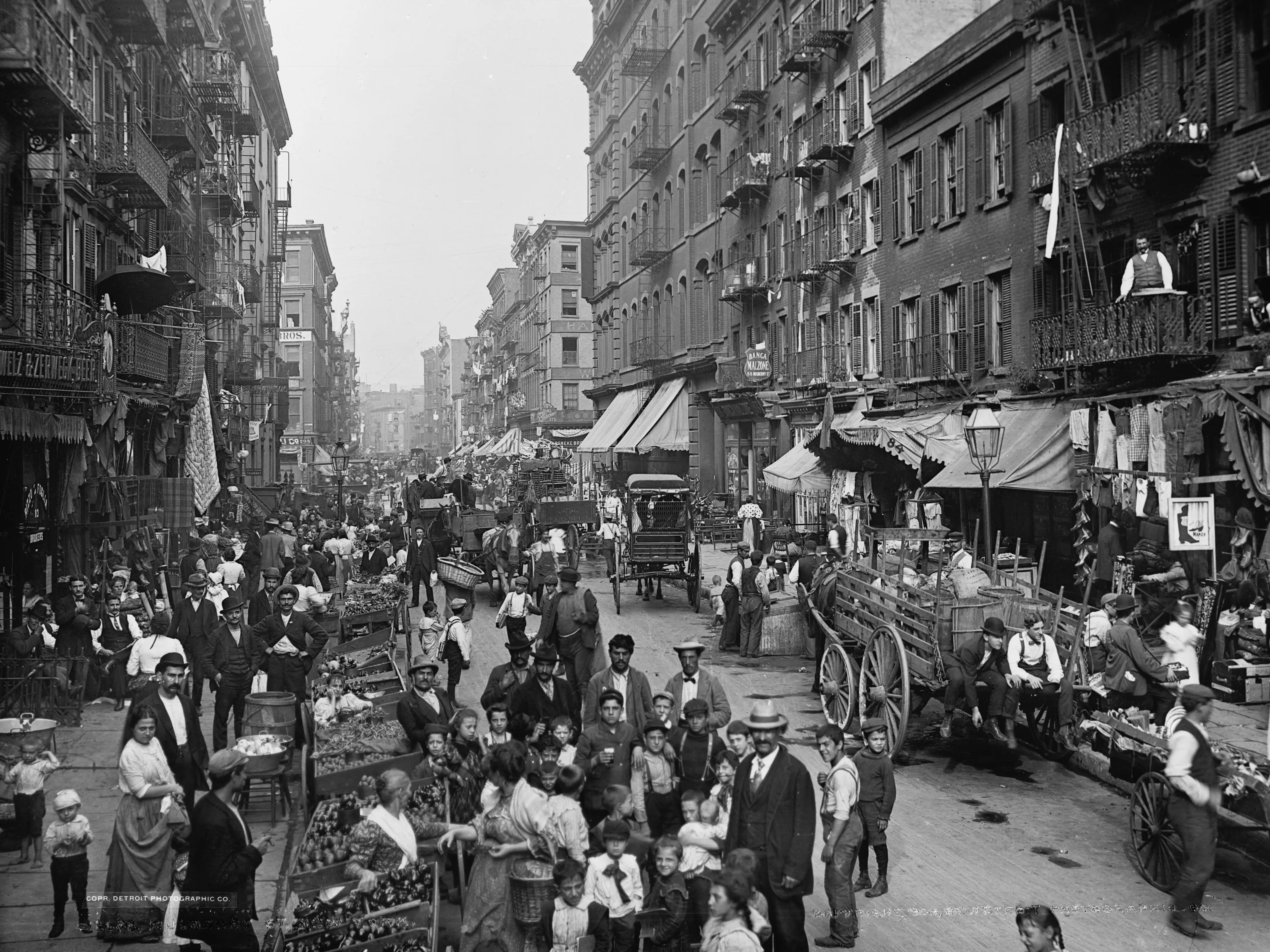 Street scene showing pedestrians, shoppers, and merchants with their vendor carts and stalls, on Mulberry Street, New York, circa 1900.