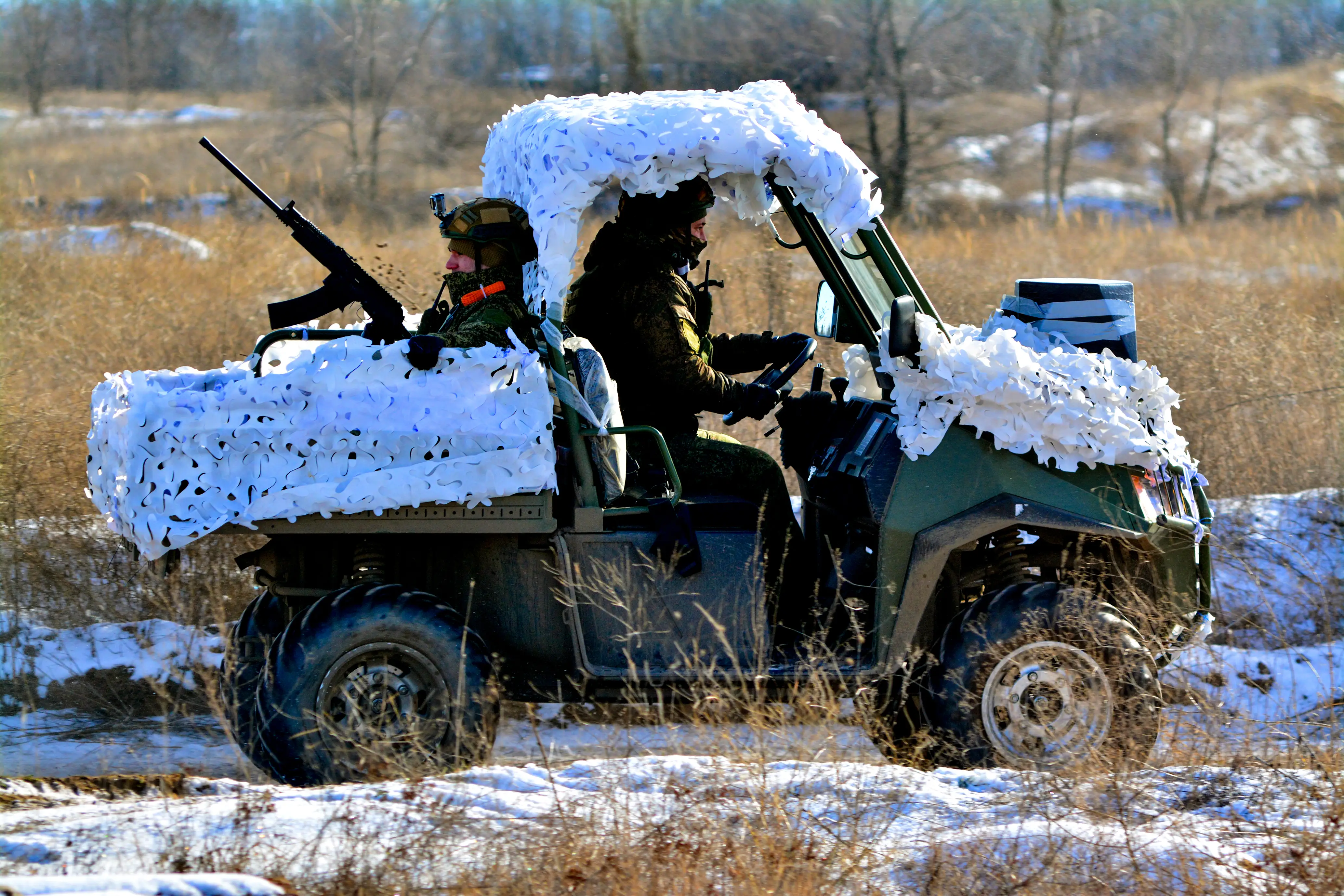 A Russian soldier sits in the back of a vehicle with a firearm as another grabs the steering wheel in the front cabin.