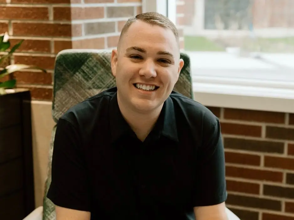 Kyle Elliott is sitting on a chair holding a phone.