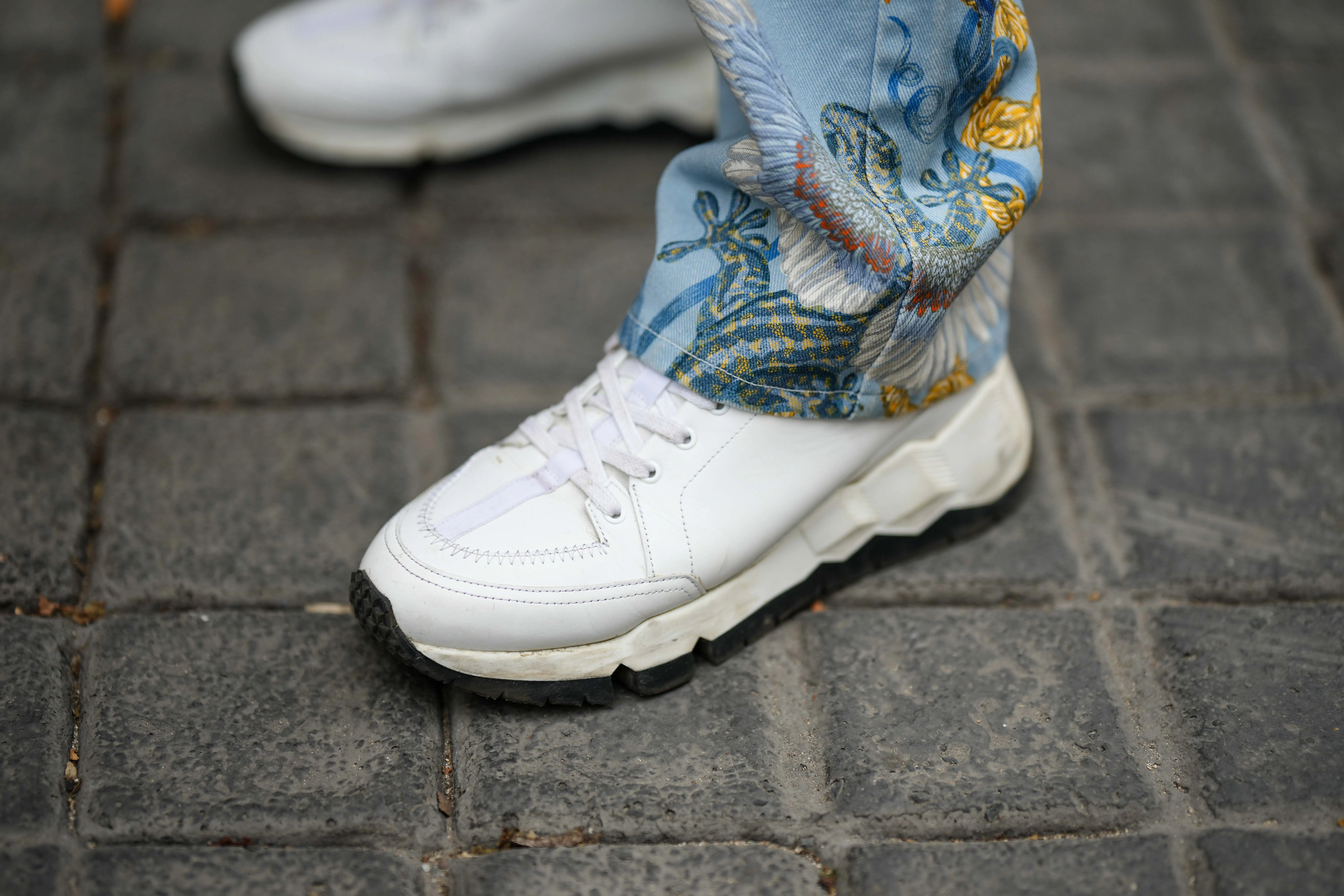 White sneaker with patterned pant leg above it on cobblestone