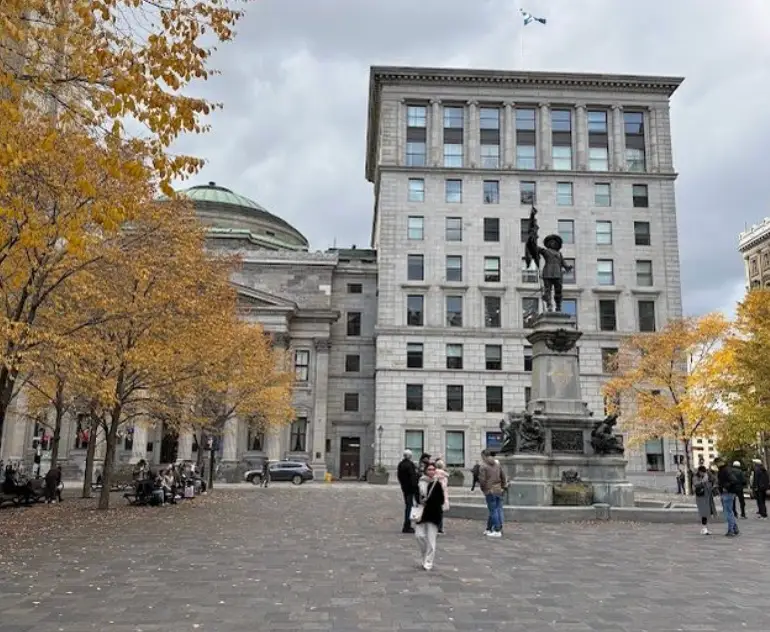 A cobblestone street, building, and statue in Montreal, with trees in the corner.