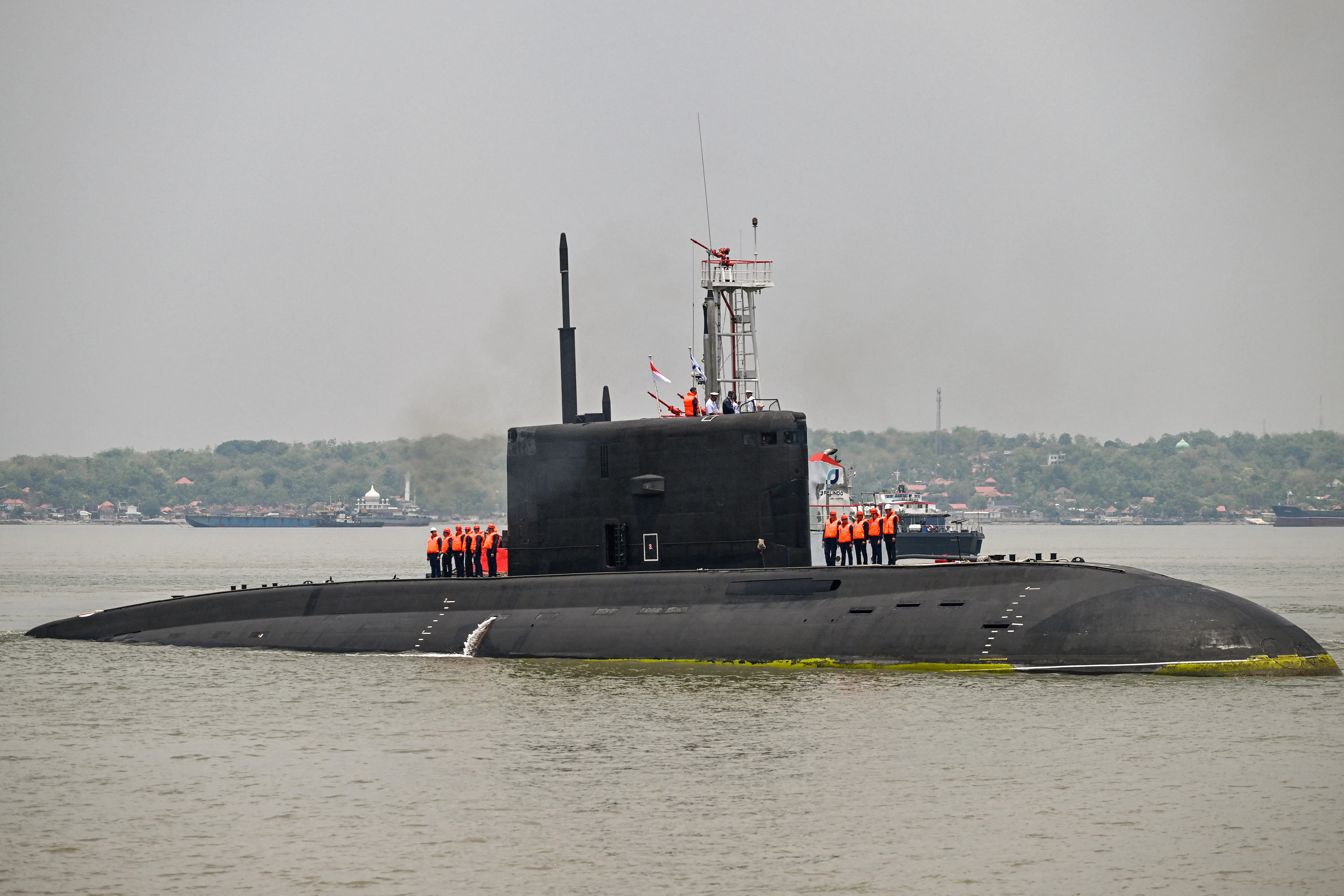 A black submarine sits in greenish-bluish water with a murky grey sky in the background.