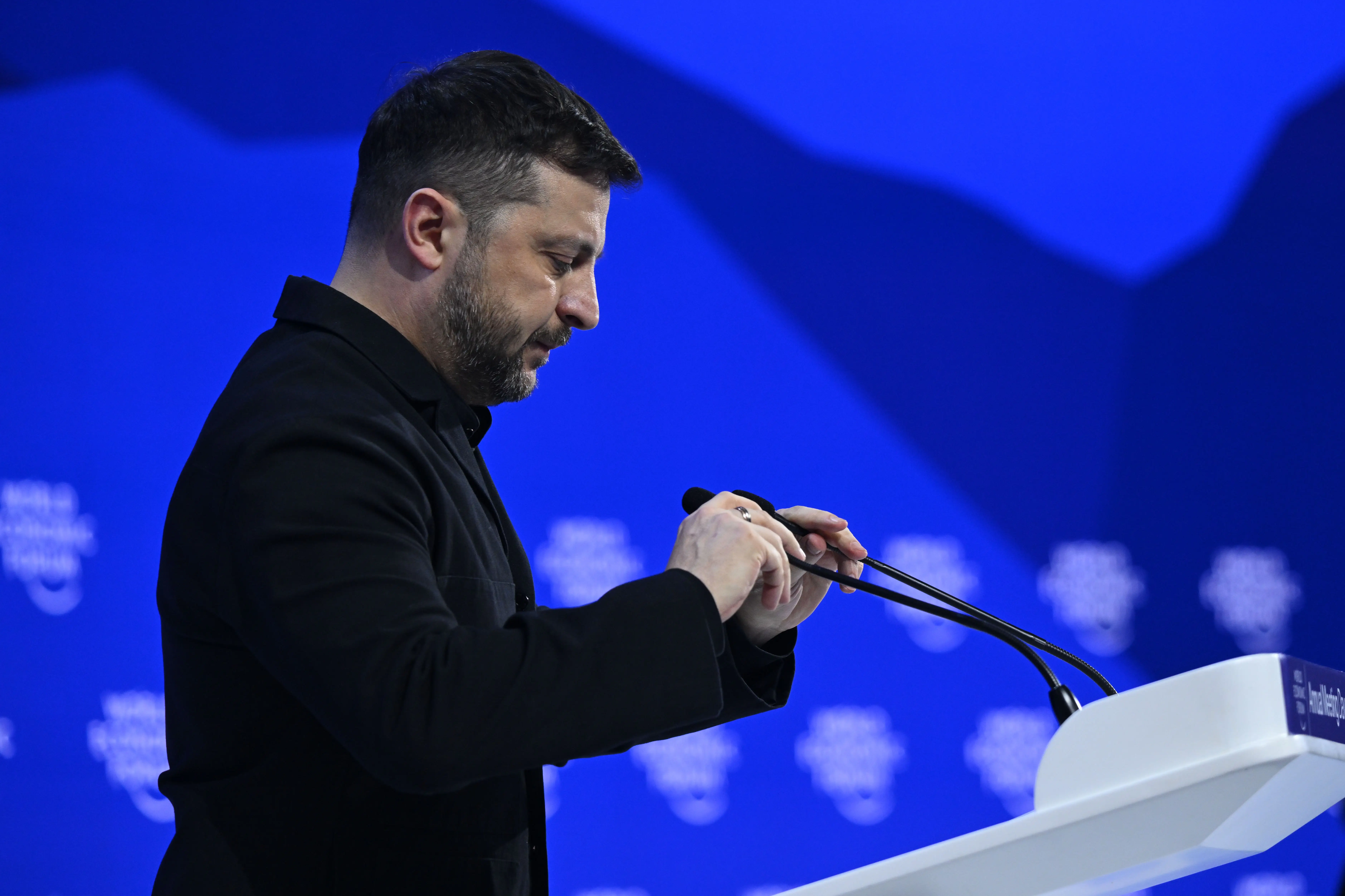 Zelenskyy adjusts rostrum mics on stage.