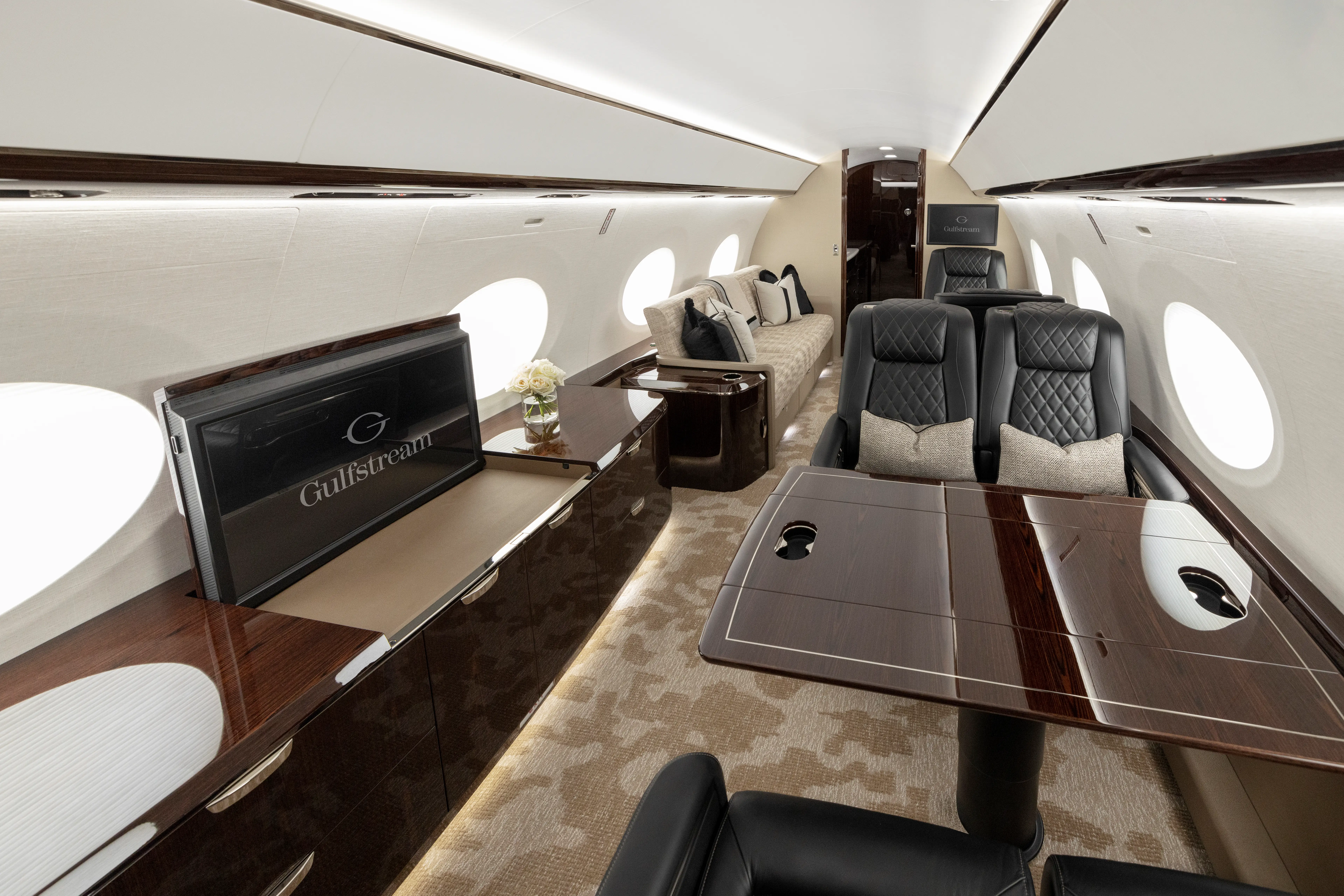 The interior of a Gulfstream G800 private jet has several leather seats, a couch, and a television.