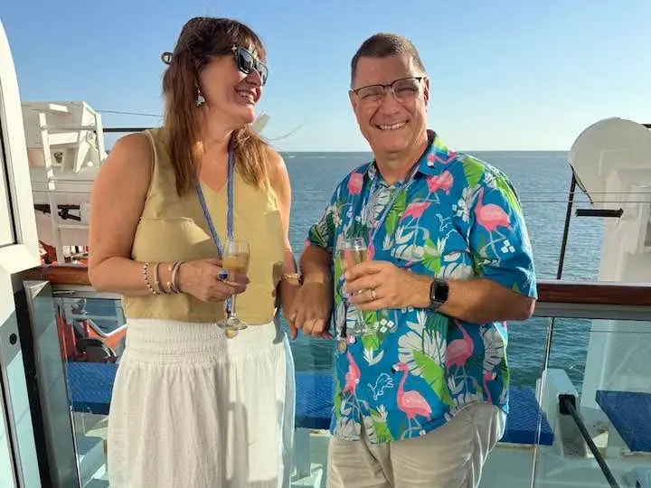 Author Jill Robbins and husband smiling with drinks on balcony on Princess Cruise
