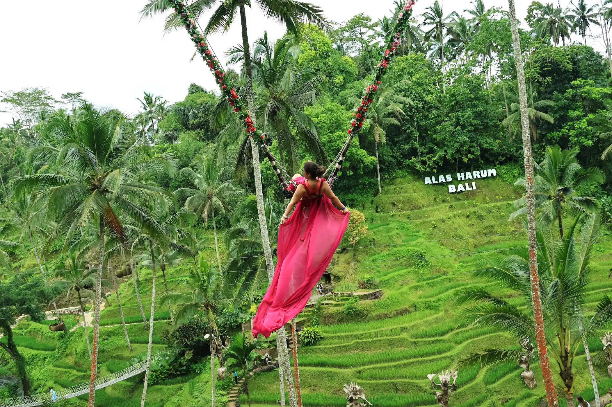 A photo of Gabby with a long piece of pink fabric on a swing over lush greenery.