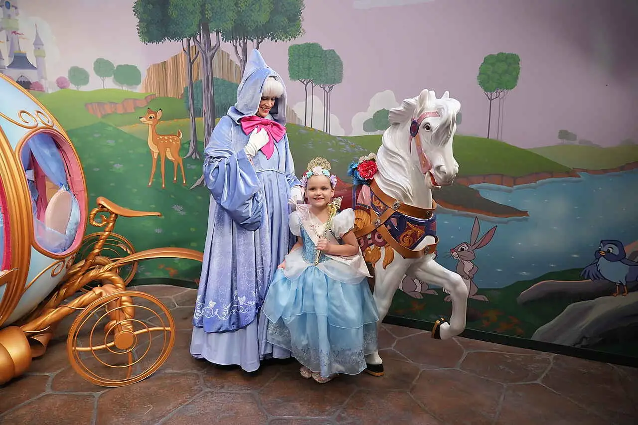 Girl in Cinderella dress with fairy godmother character in front of movie backdrop