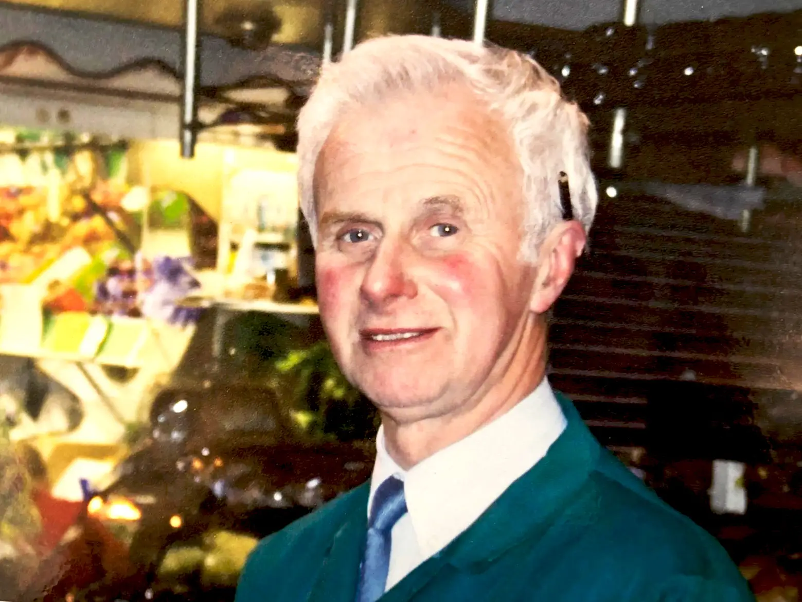 An older man in a tie in front of a grocery stand.