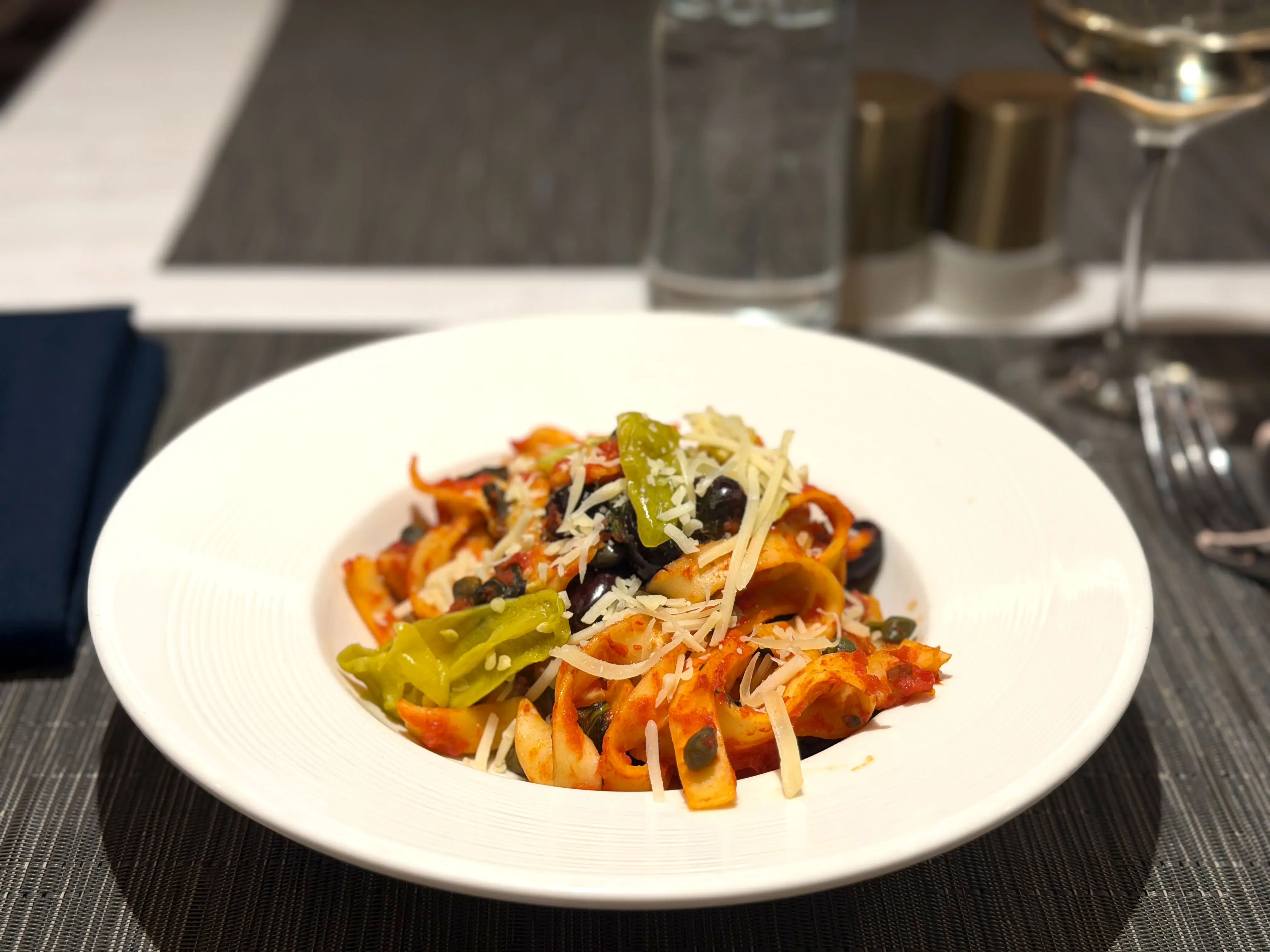 A plate of tagliatelle pasta with peppers, olives, and cheese.