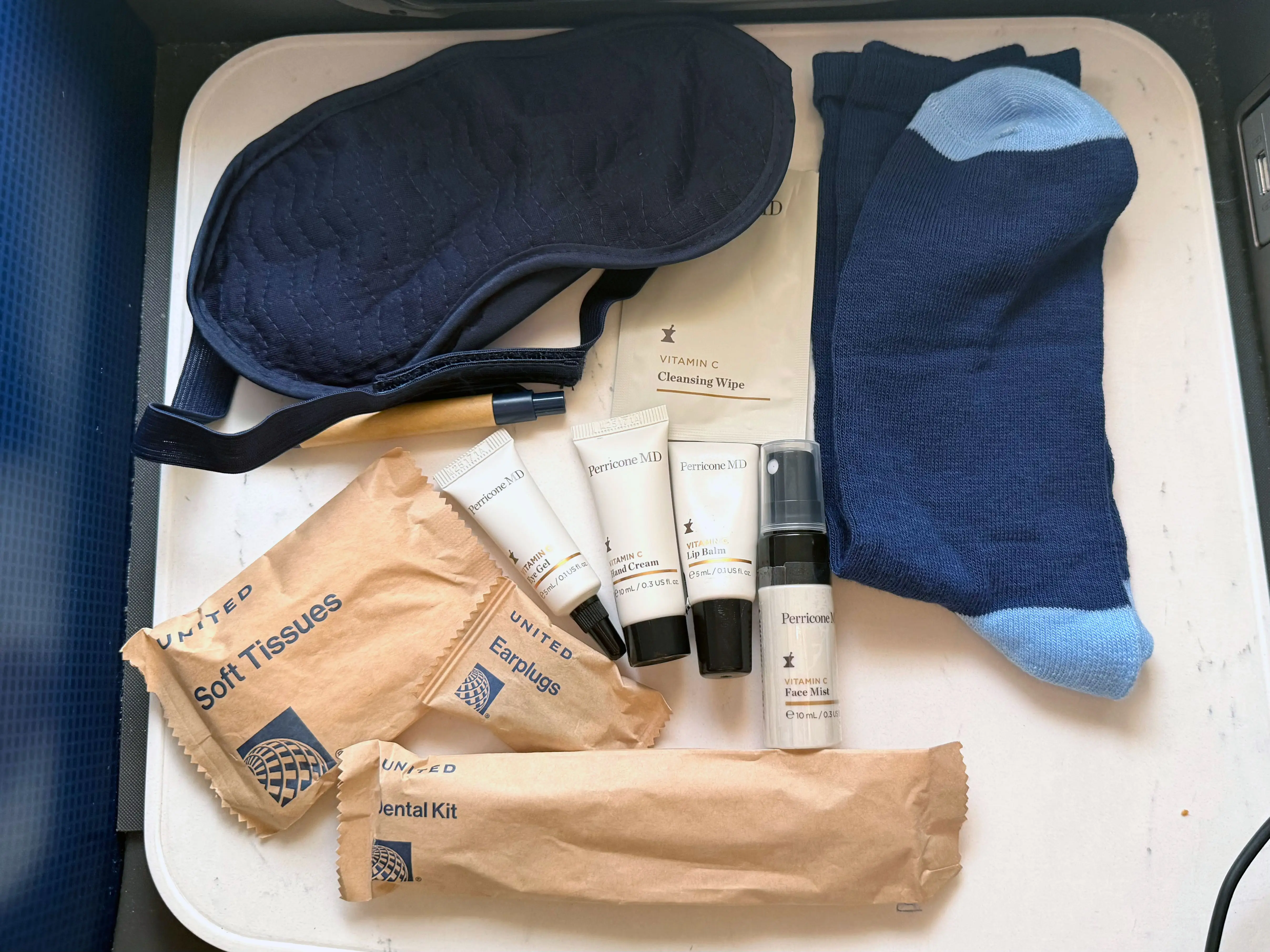 An eye mask, socks, skincare items, a dental kit, tissues, and earplugs on a plane tray.
