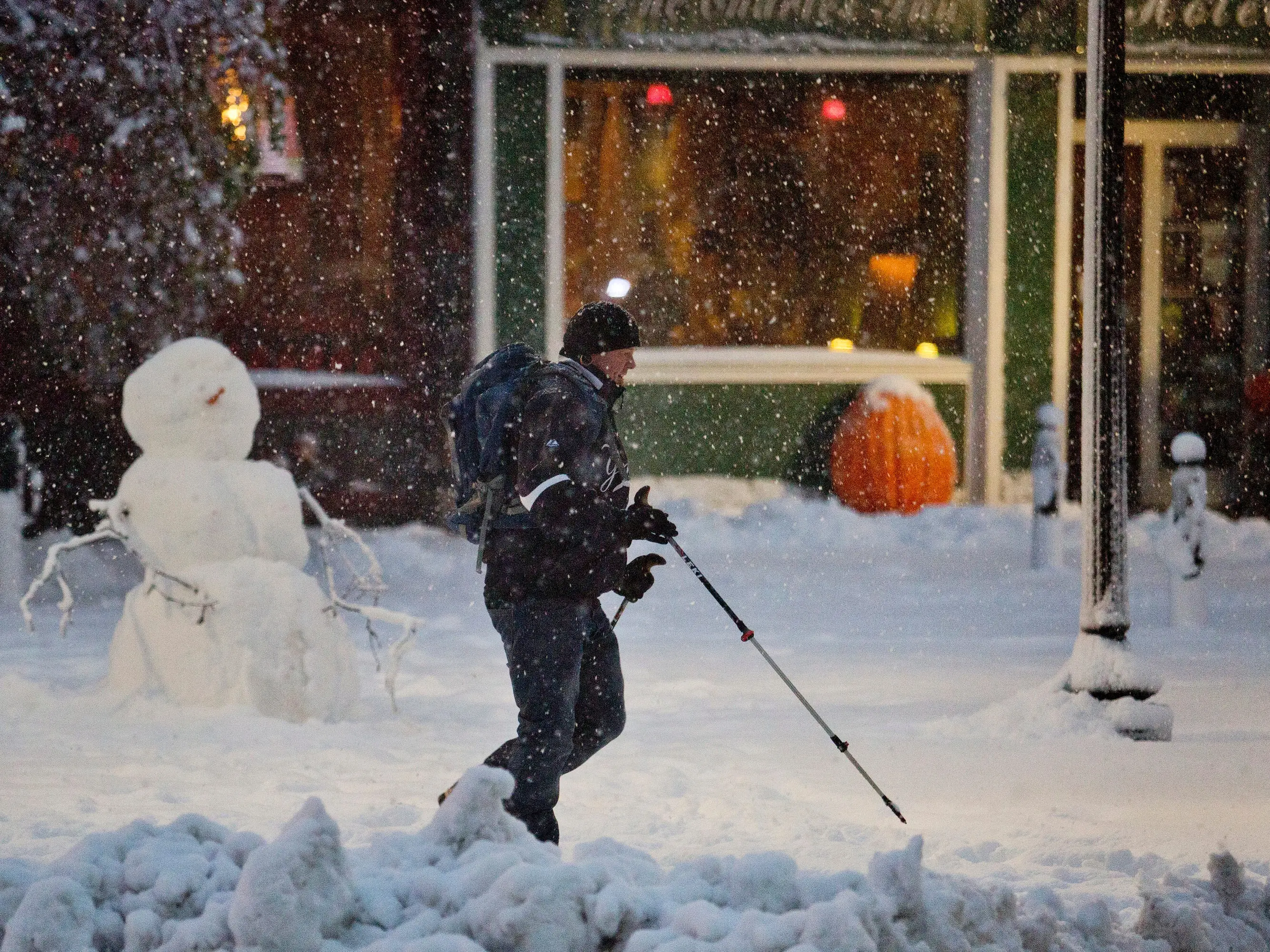 A man uses ski poles to help him walk past a snowman in downtown Bangor Sunday, November 2, 2014, after an early season snowstorm slapped parts of Maine including Bangor with multiple inches of snow Sunday, November 2, 2014.