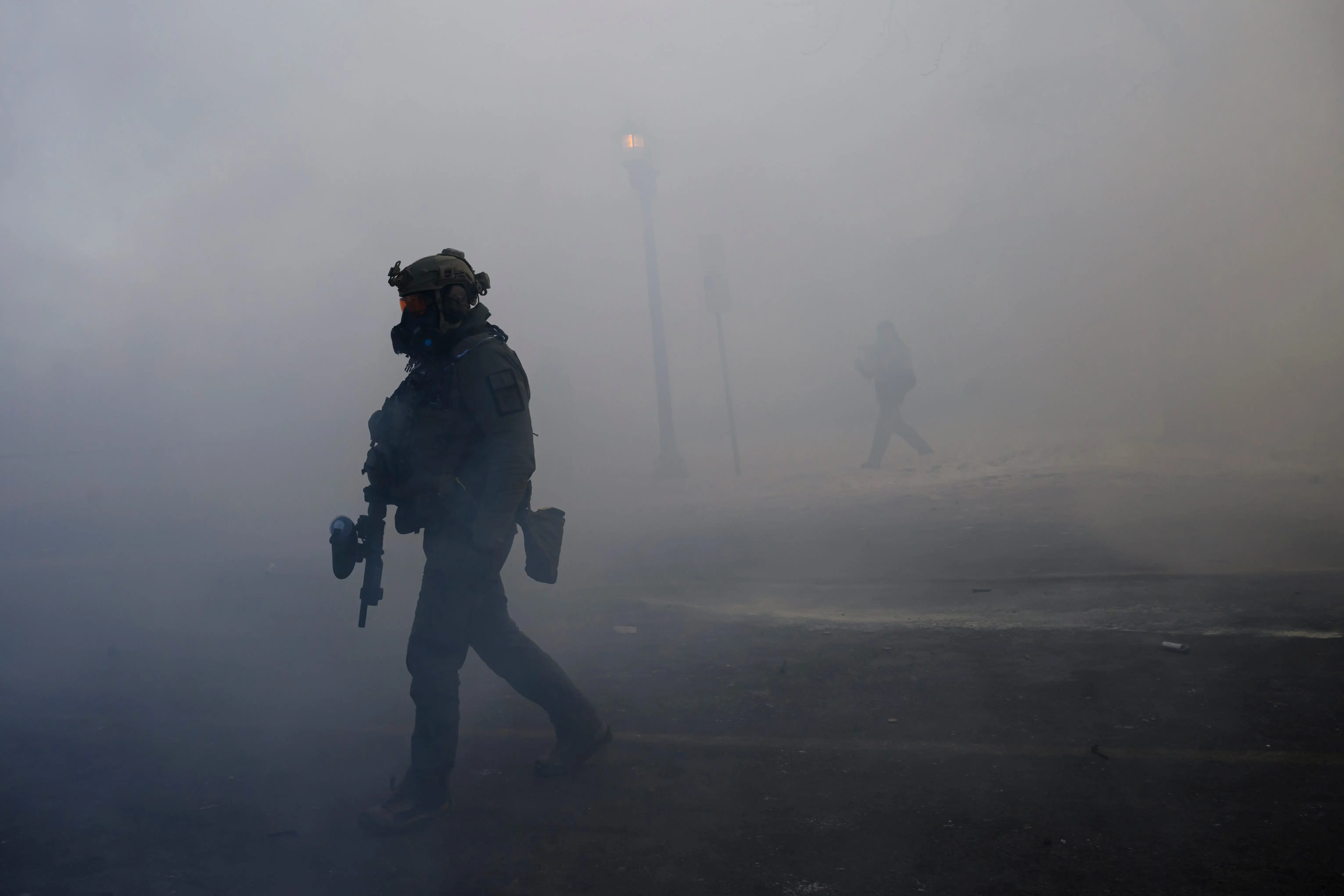 The silhouette of a federal agent walking through the street surrounded by tear gas smoke.