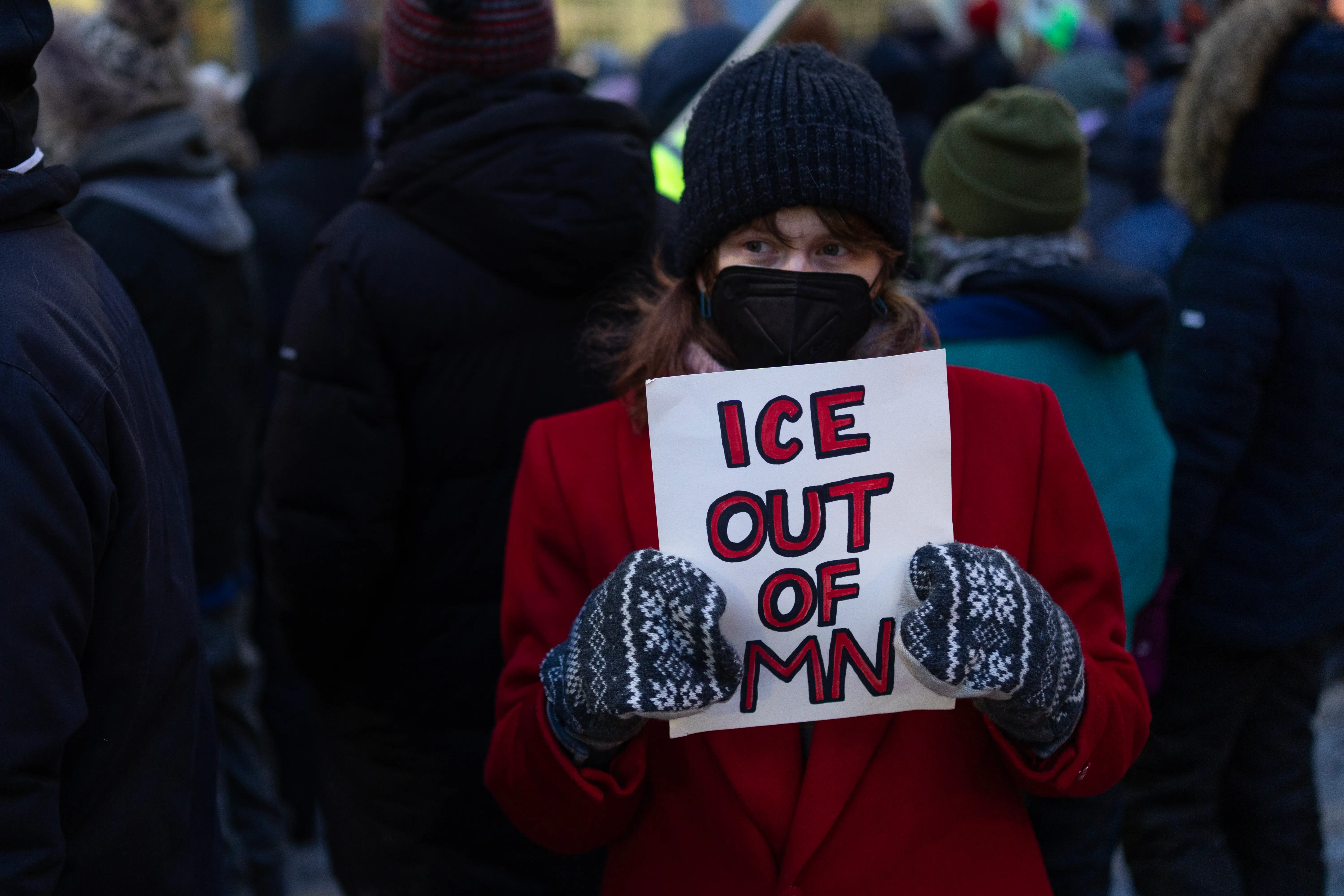 A protester in red coat and mittens holds a sign reading 