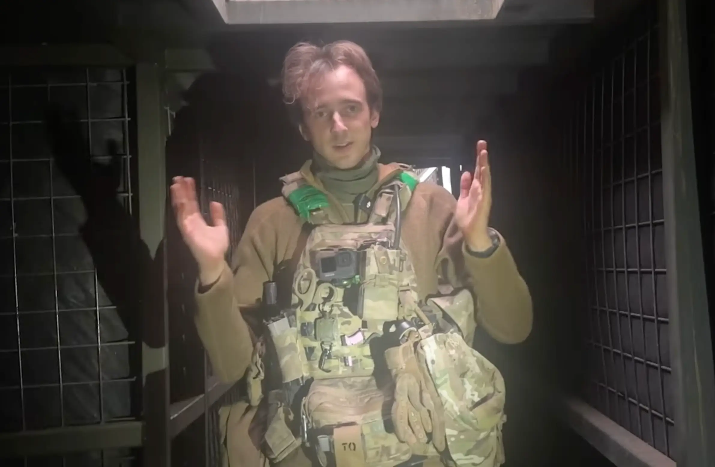 A man in khaki gear stands in an underground position wearing body equipment that has pockets and pouches, with gear like scissors and a GoPro visable