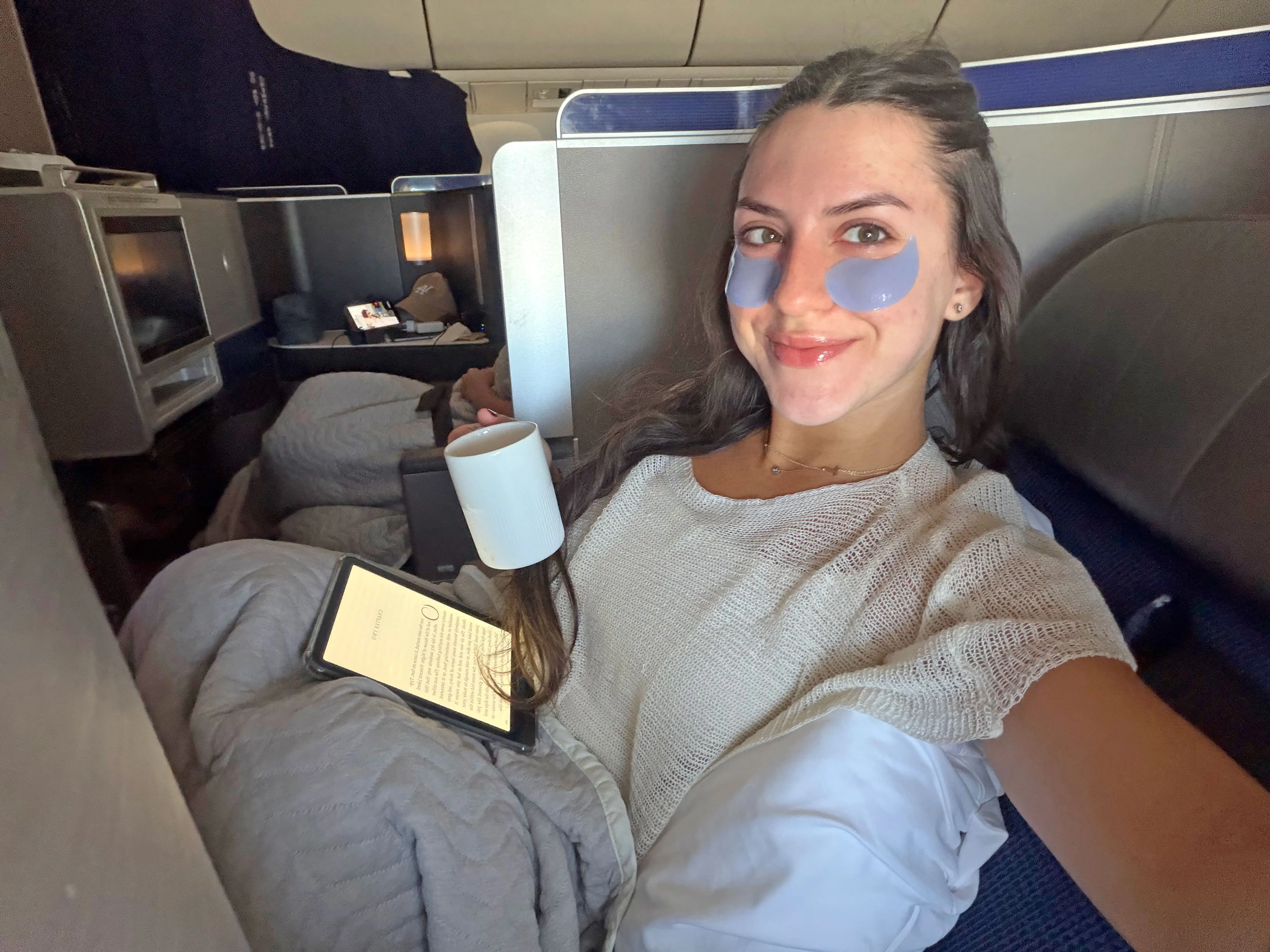 Amanda wears under-eye patches and reads on a Kindle while holding a coffee cup.