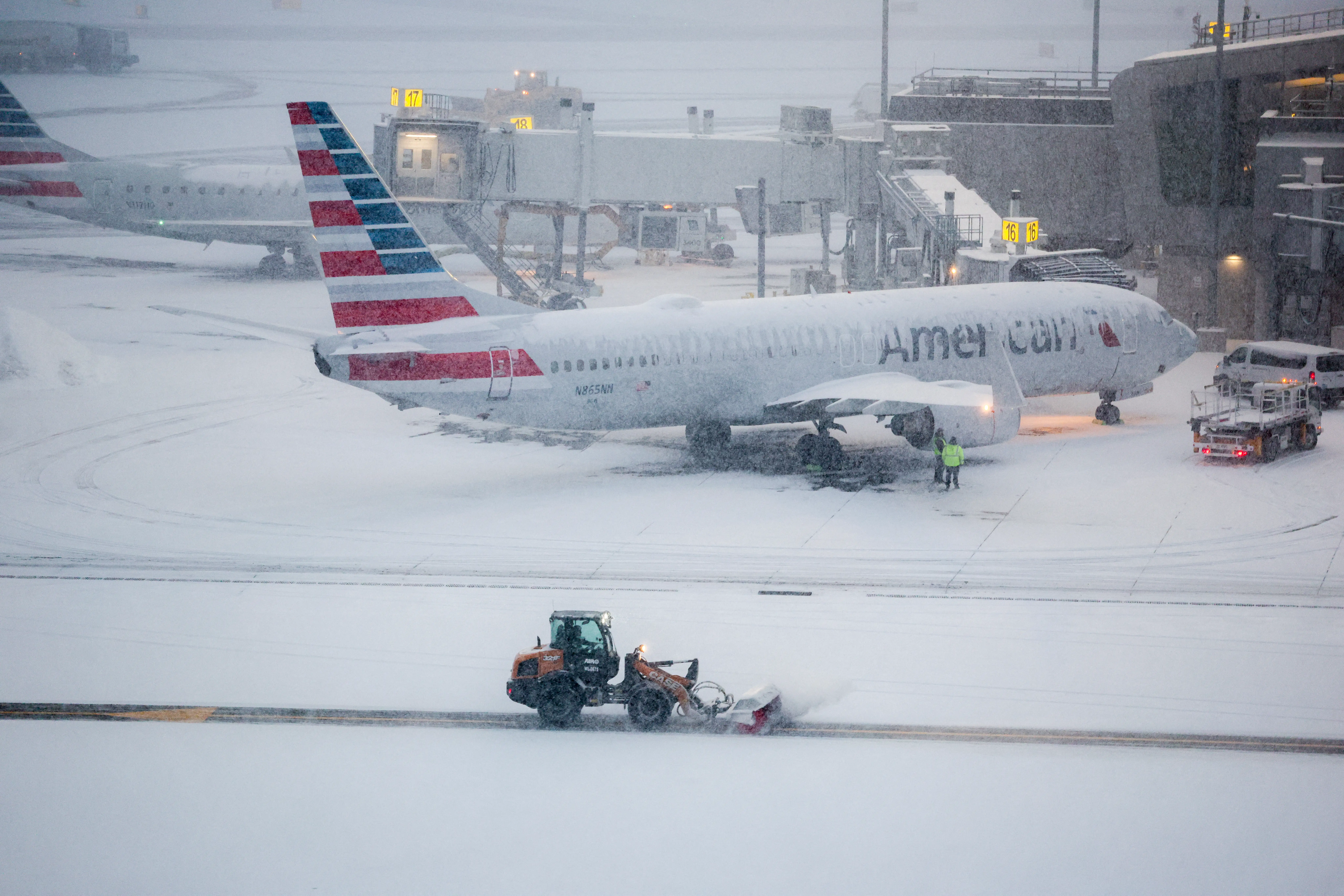 A snow removal machine is seen working while a Boeing 737 American Airlines passenger aircraft is parked at gate on the tarmac of LaGuardia airport in New York on January 25, 2026