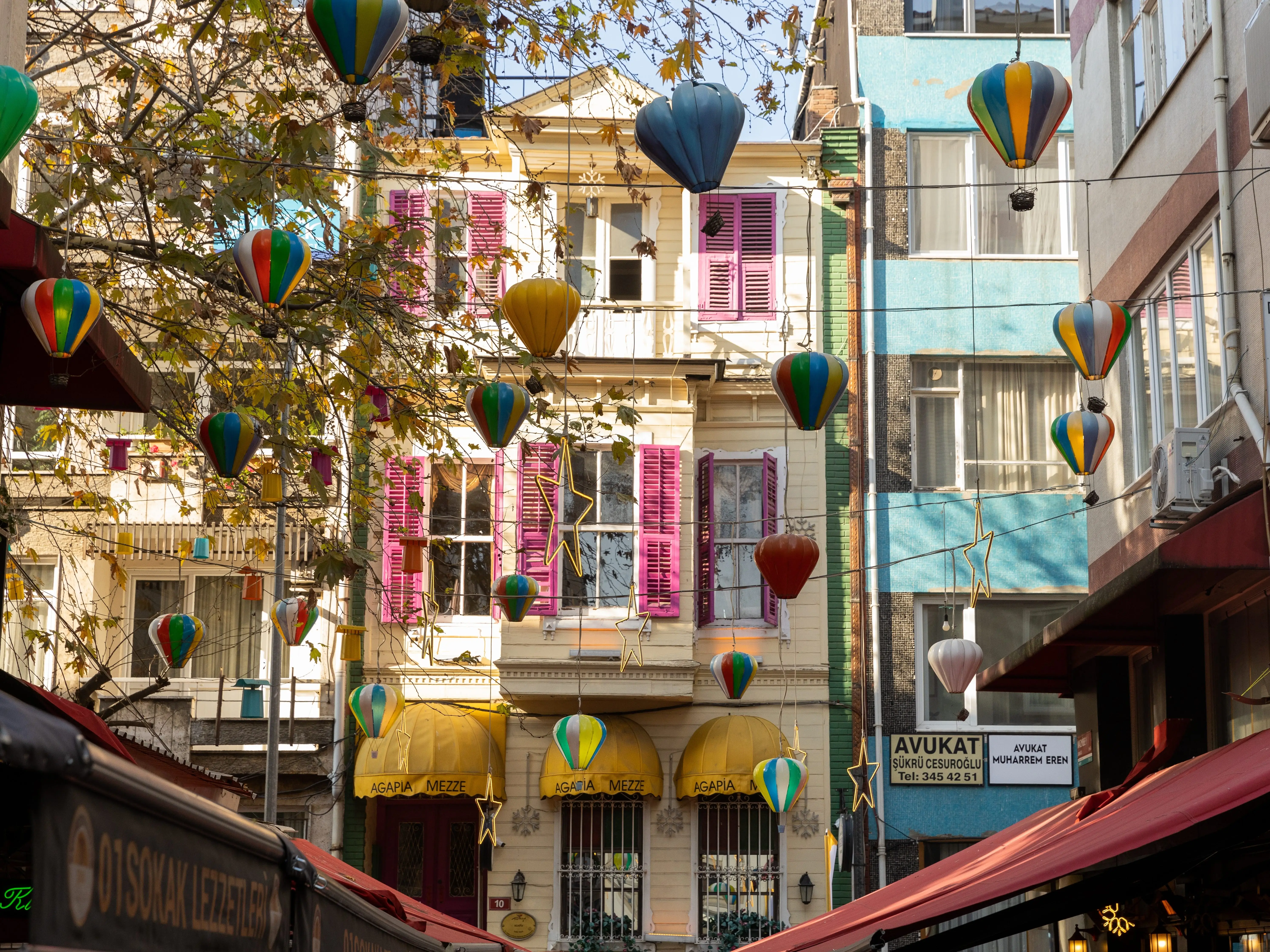 Small hot air balloons strung on wires over a street, with colorful apartments in the background.