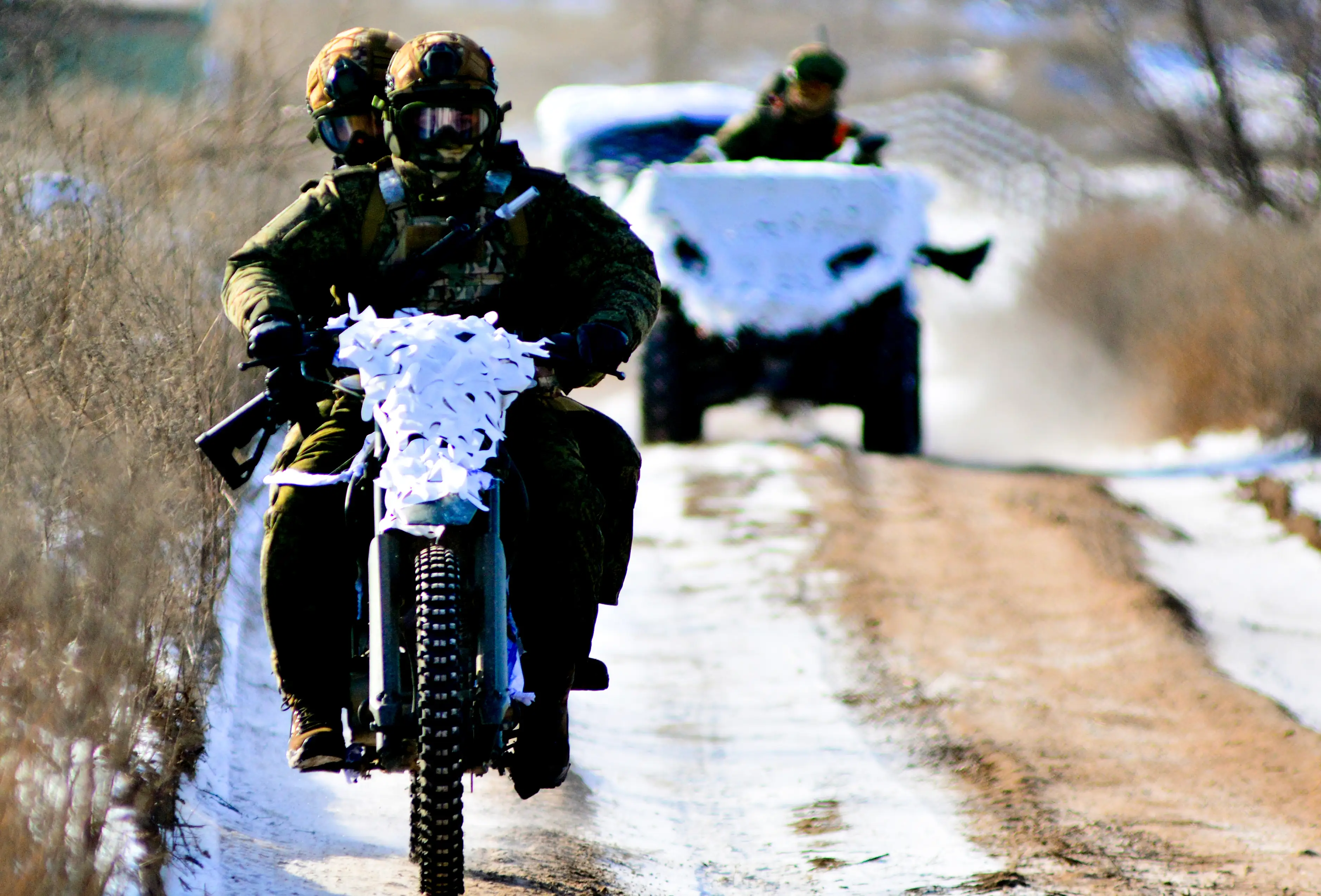 Two Russian soldiers ride on a motorbike coverd in winter camo netting.