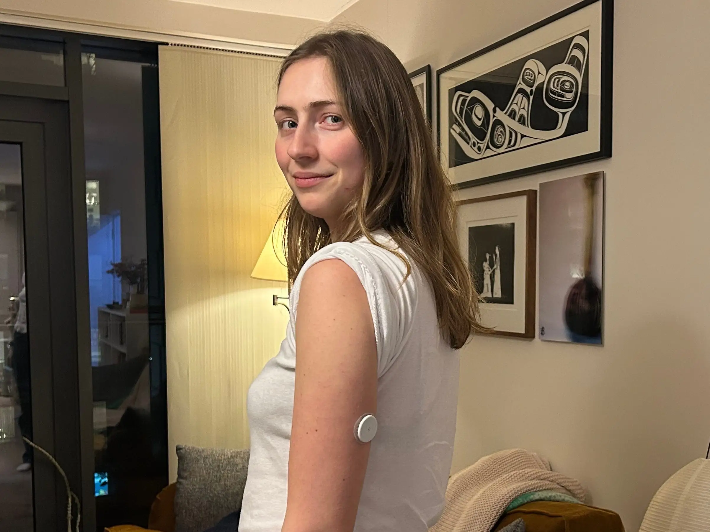 A woman wears a continuous glucose monitor on the back of her left arm.