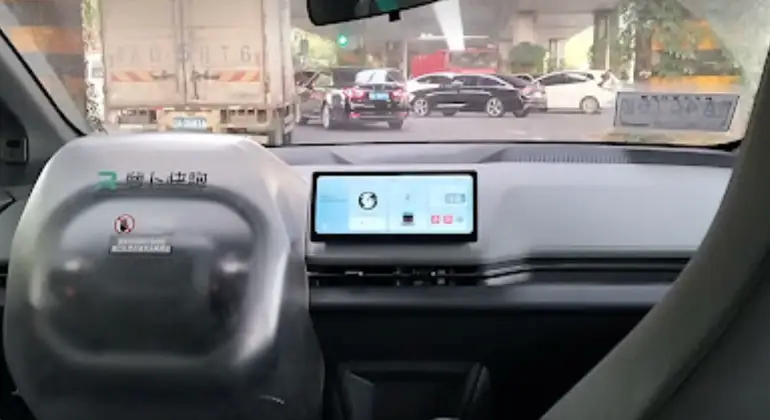 Dashboard of a Baidu Apollo robotaxi turning at a complex intersection in Wuhan, with the steering wheel covered to prevent misuse by passengers.