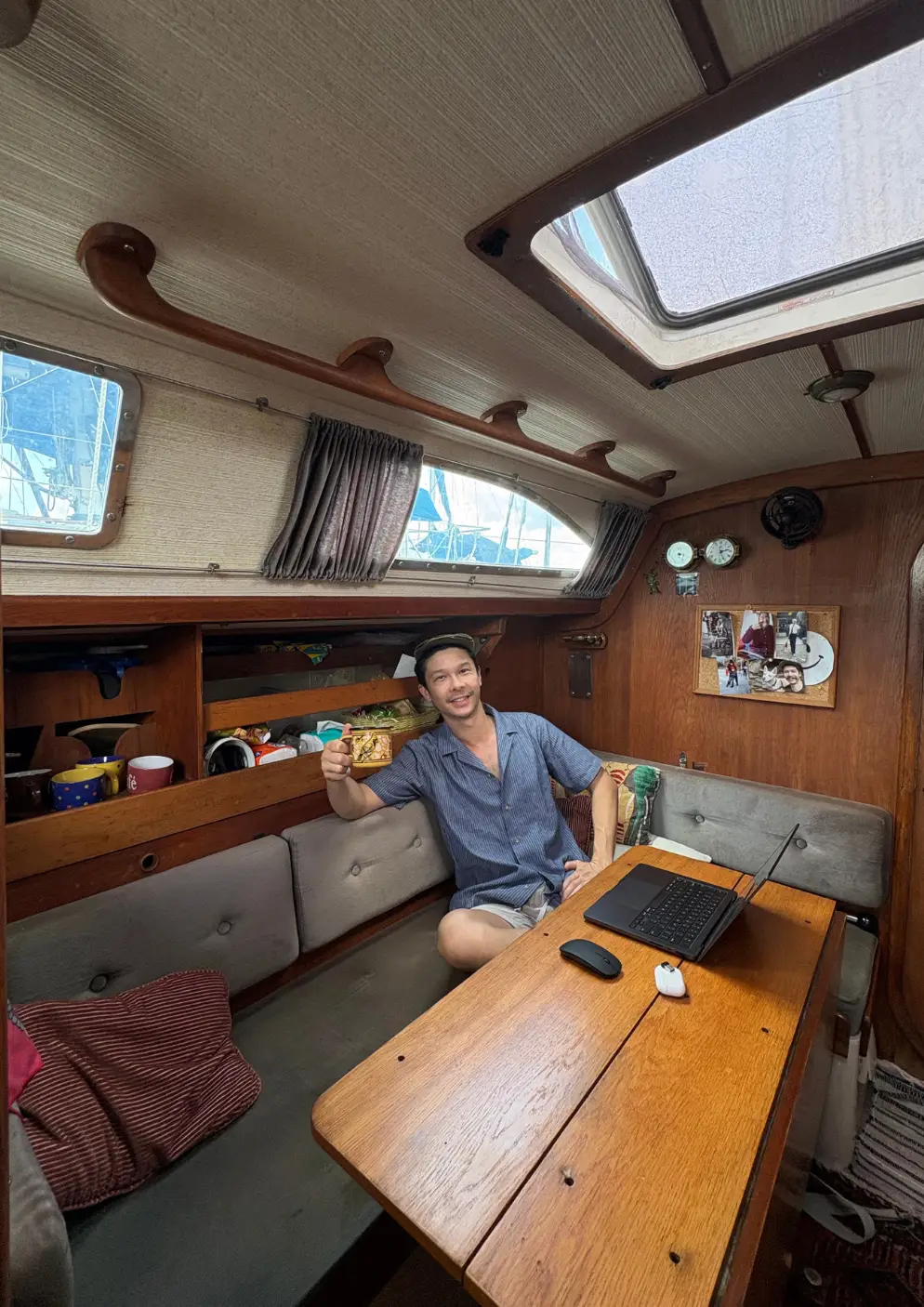 Jeremy Brand Yuan sitting inside his boat, working at a table with his laptop in front of him.