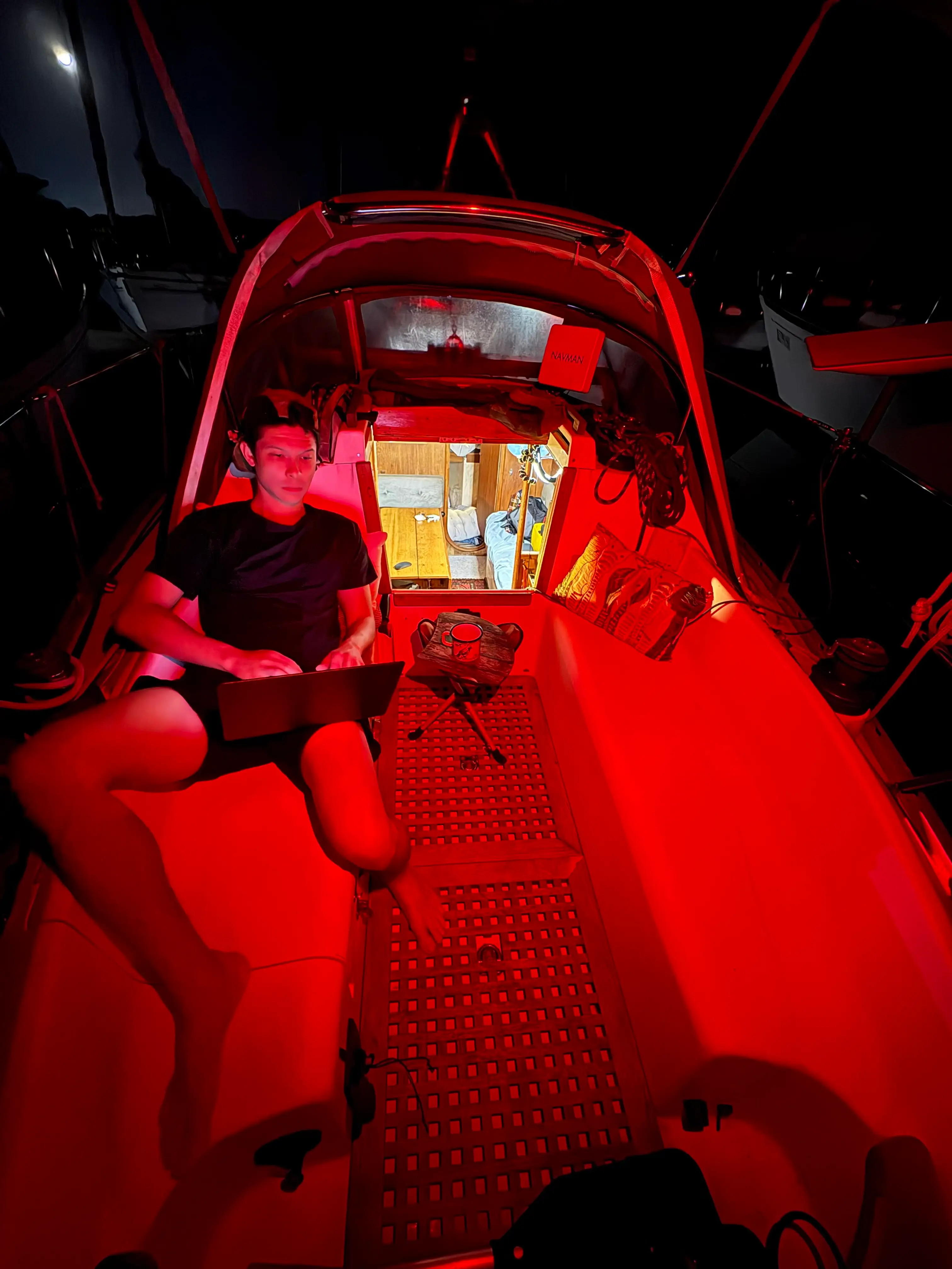 Jeremy Brand Yuan is working from his boat at night, there is a red light illuminating his workspace.