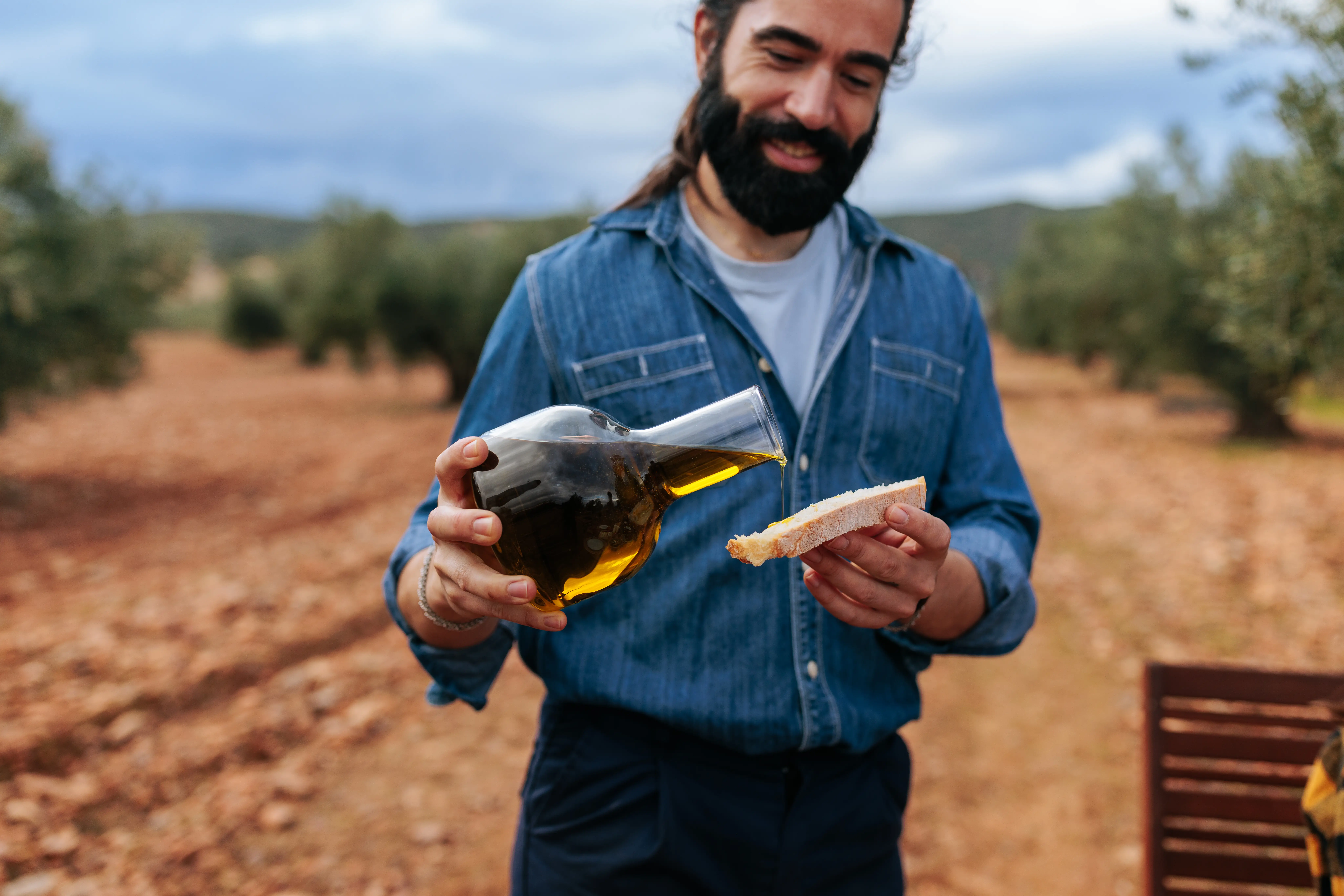 A farmer is pictured pouring olive oil onto a slice of bread.