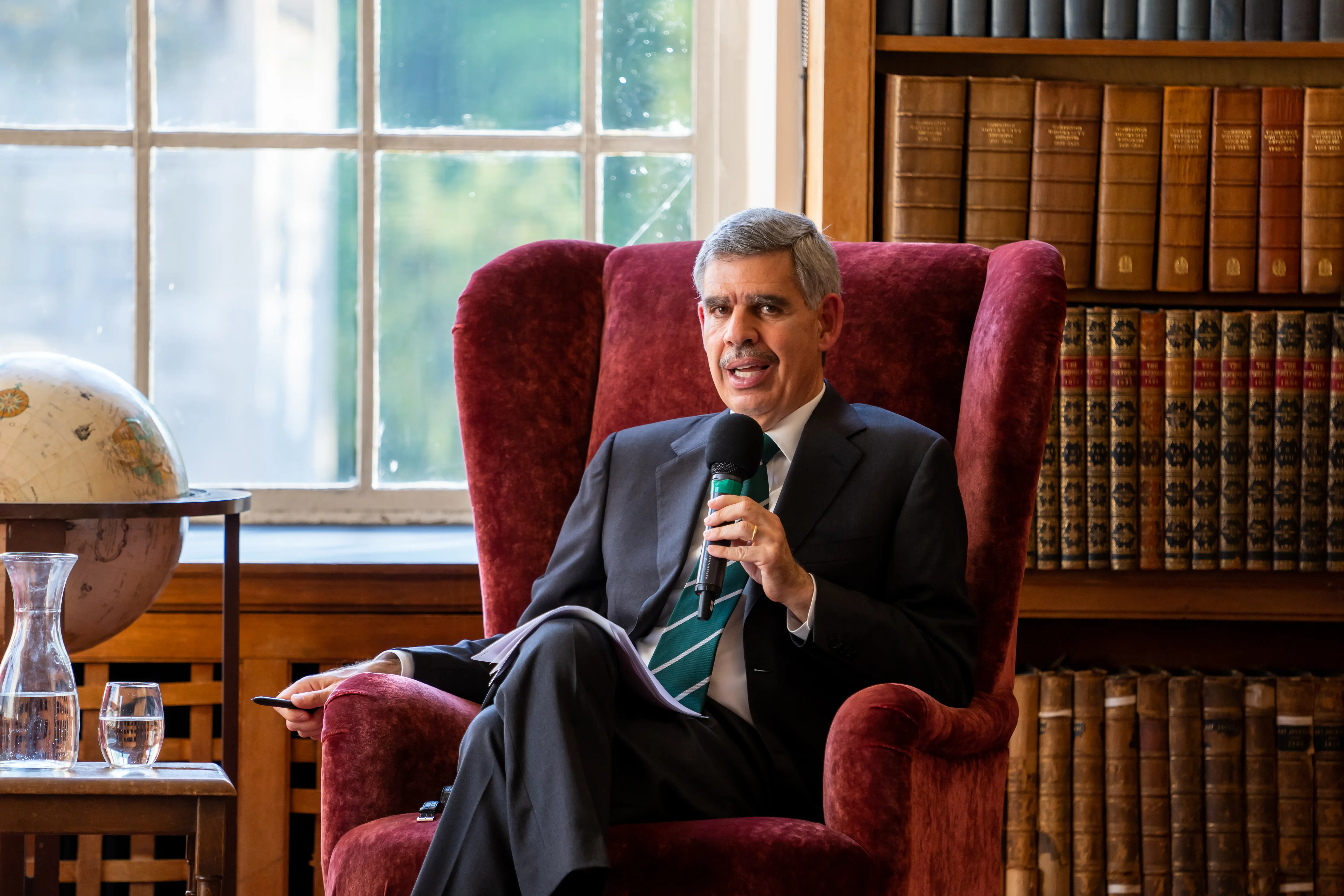 PIMCO former CEO/co-CIO,  professor at Wharton Mohamed El-Erian speaks while sitting on a chair while reading with the mic.