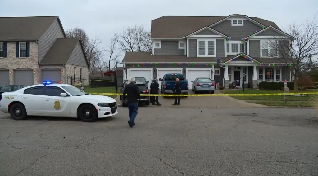 A police vehicle, officers, and yellow crime scene tape in front of a house.