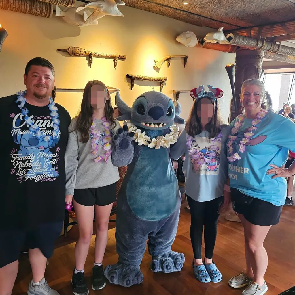 A family of four with blurred faces posing with Stitch from Lilo & Stitch.