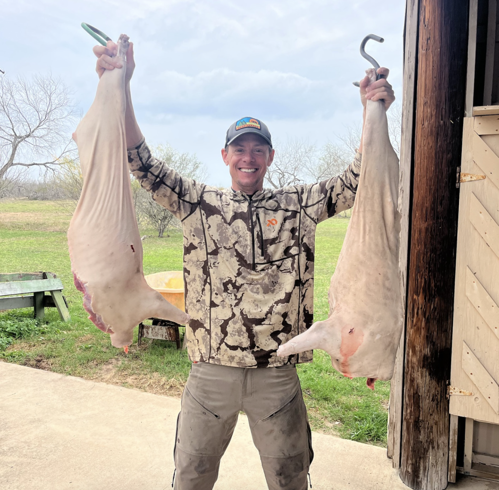 Steven Rinella holding up two hunted pigs.