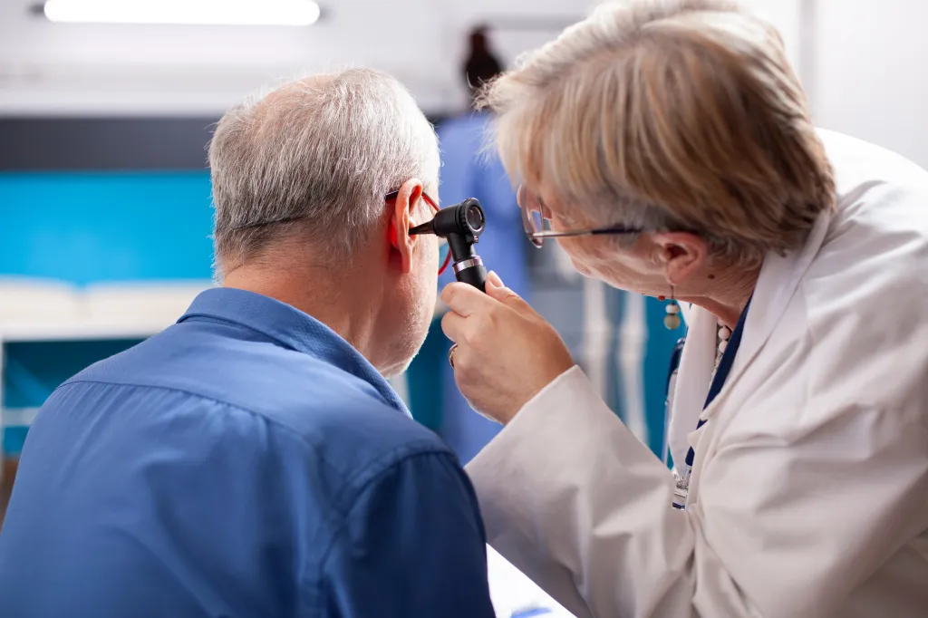 Doctor performing a hearing test on an older man with an otoscope.