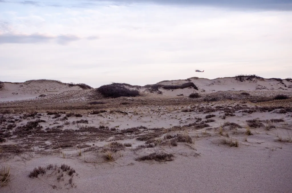 Helicopter flying over sand dunes and sea grasses at Cape Cod National Seashore.