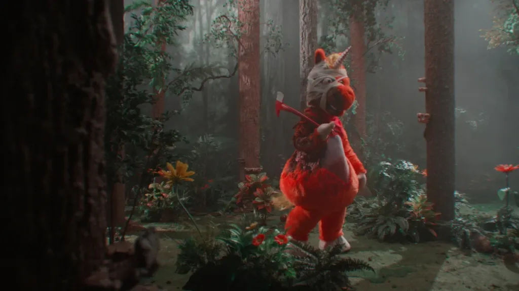 An orange uniform mascot costume stands bandaged and bloody in the woods with an ax