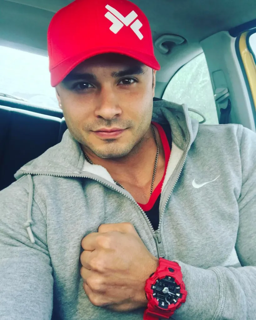 Christian Bueno wearing a red cap and grey hoodie, posing for a selfie.