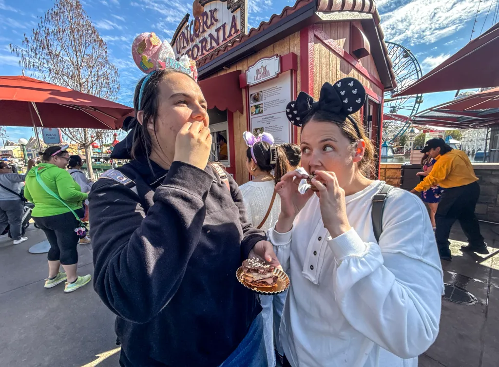 Two women in Minnie Mouse headbands eat desserts from Uncork California at Disneyland.