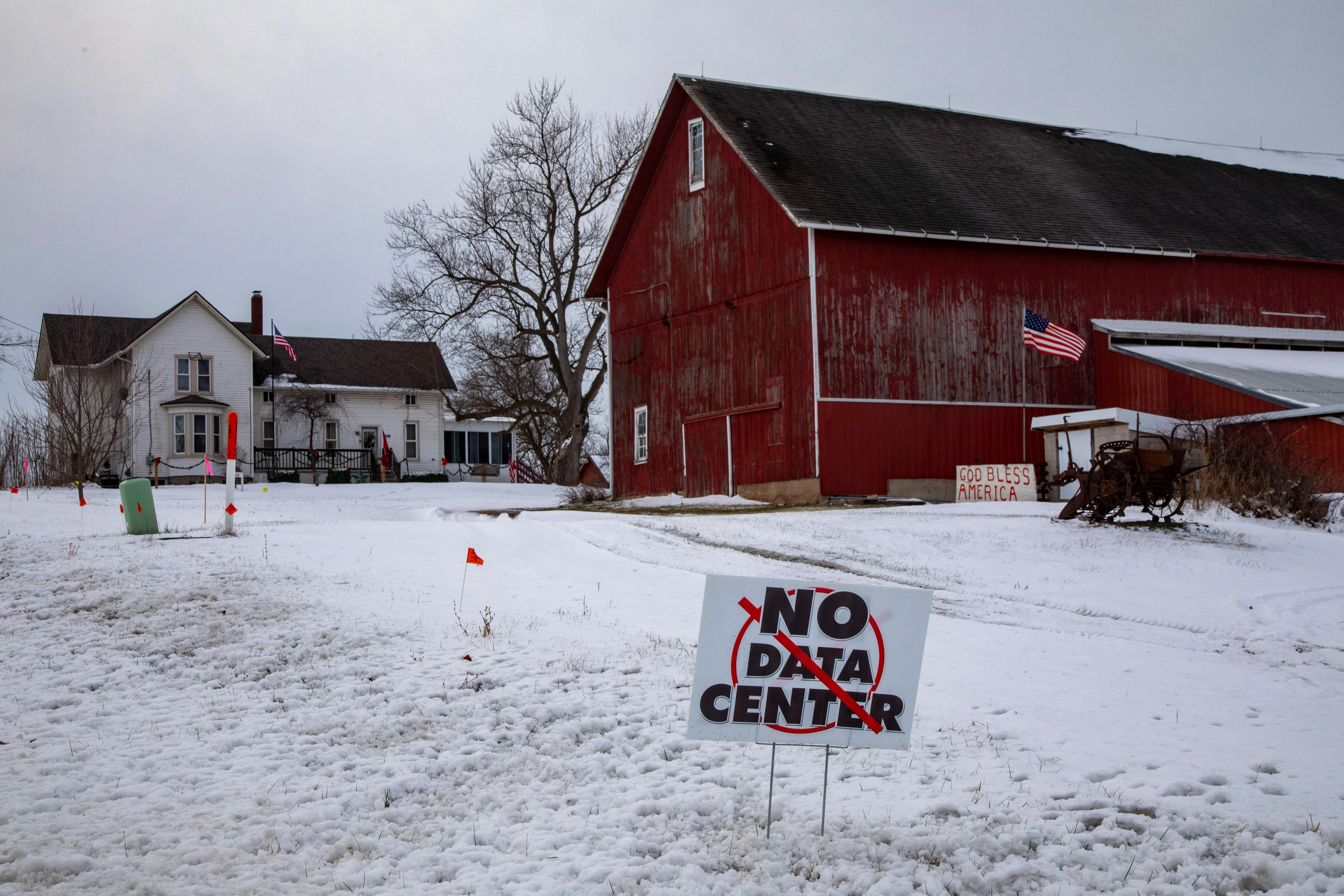 A sign that reads No Data Center sits on a snowy lawn in front of a farm