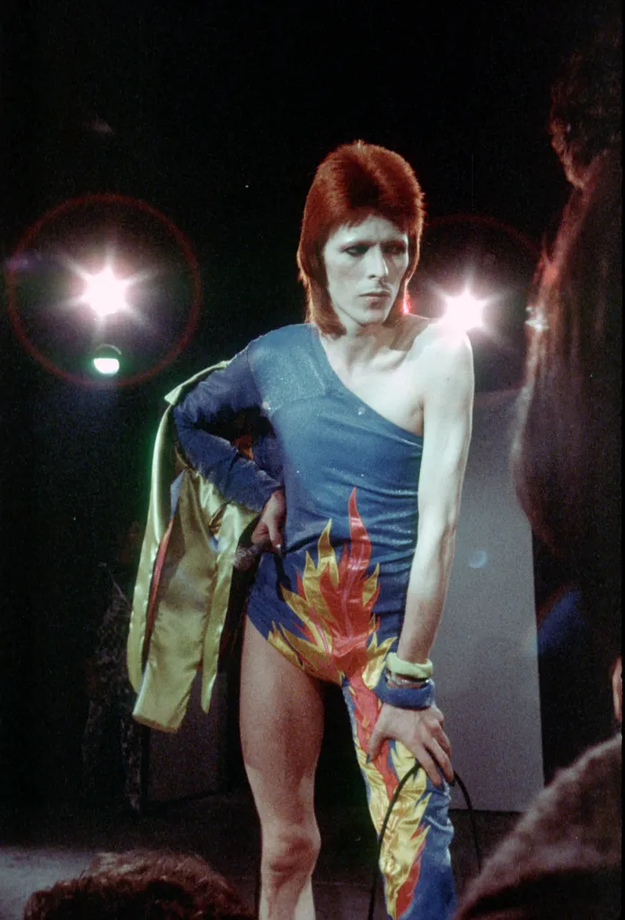 David Bowie in a blue one-piece costume with red and yellow flames.