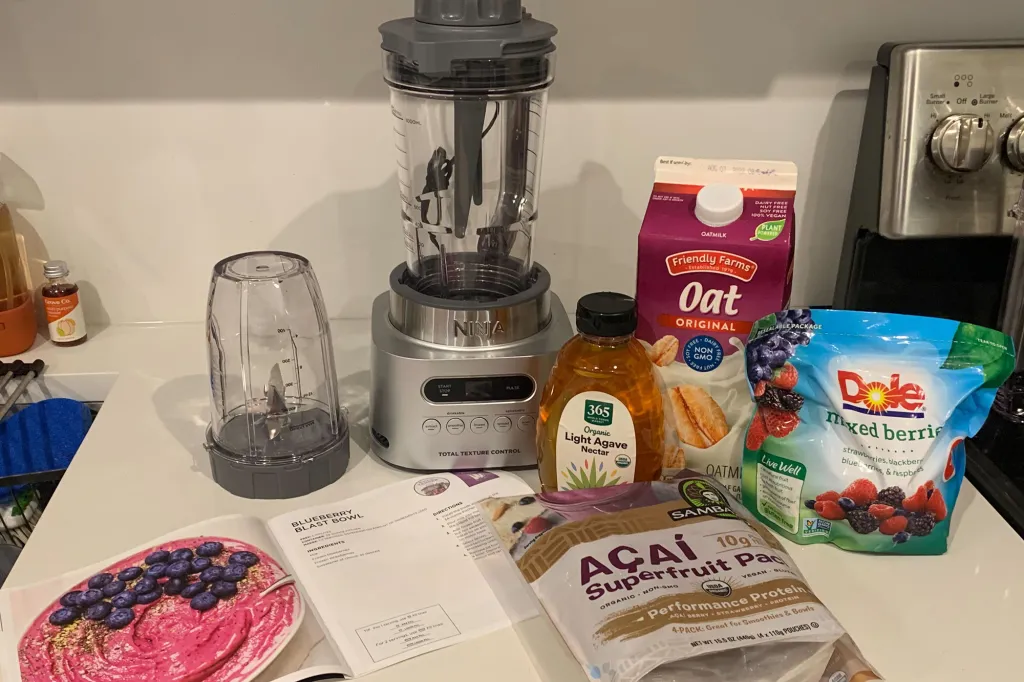 A blender on a counter with two other cups and groceries
