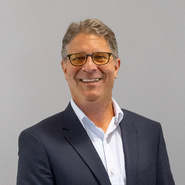 Headshot of James R. Wacht, a smiling man with glasses, light brown hair, and a navy suit over a white shirt.