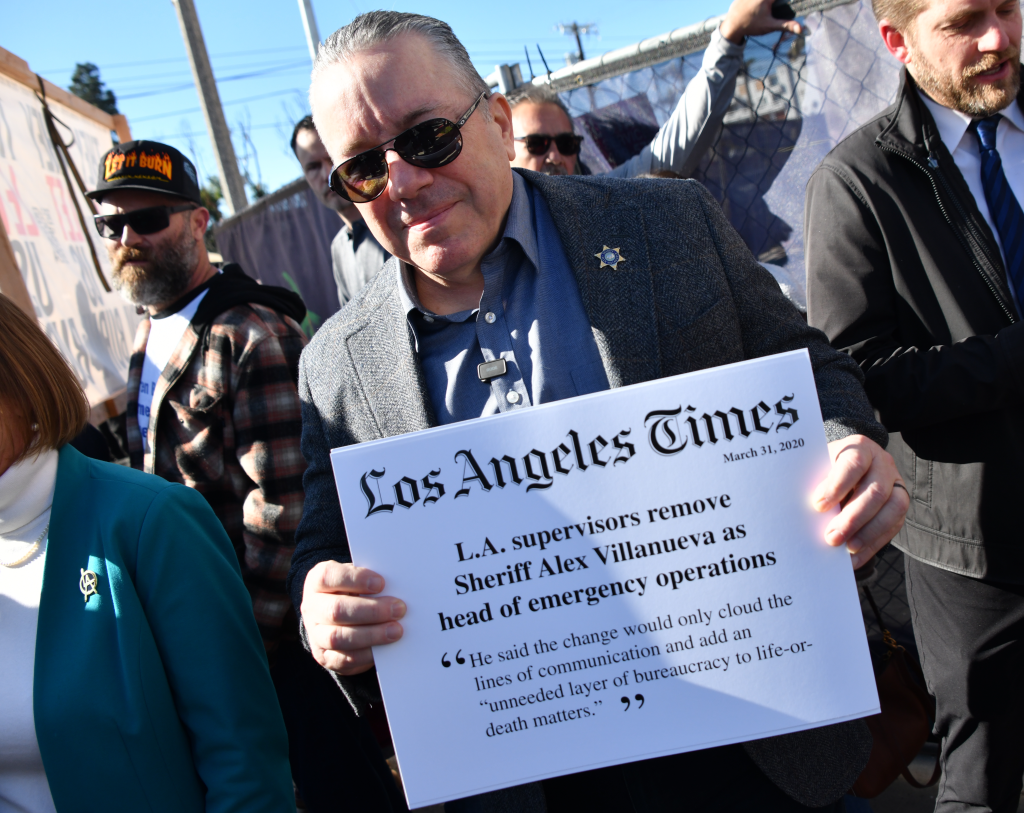 A man in sunglasses and a jacket holds up a sign that reads 