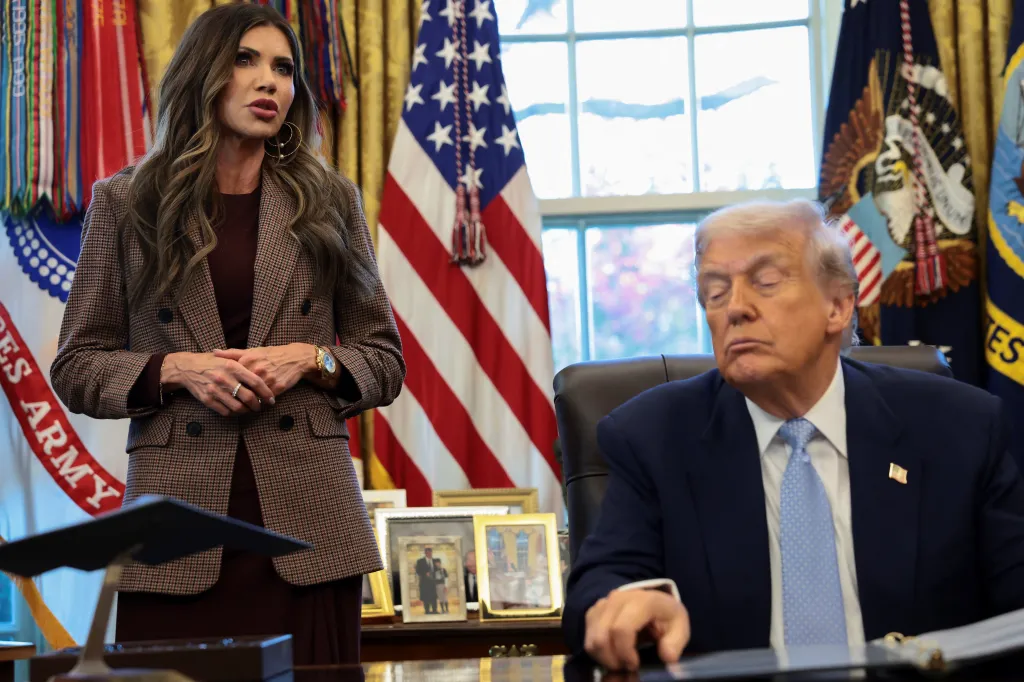 President Trump sits while Homeland Security Secretary Kristi Noem stands by his side, as he meets with the White House Task Force on the FIFA World Cup 2026 in the Oval Office at the White House in Washington, DC, on Nov. 17, 2025.